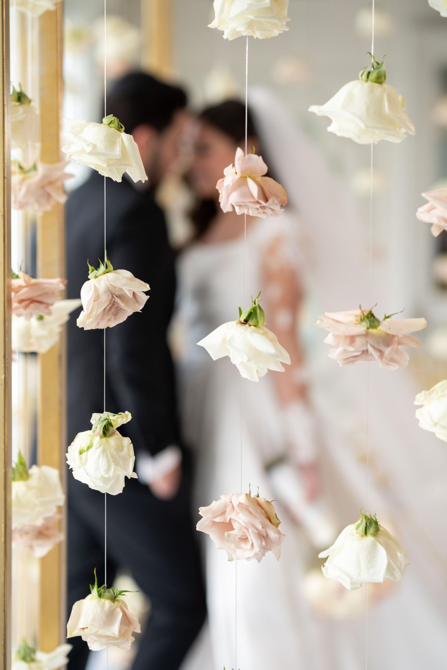 Delicate pink and white roses suspended on strings create an ethereal wedding decoration display.