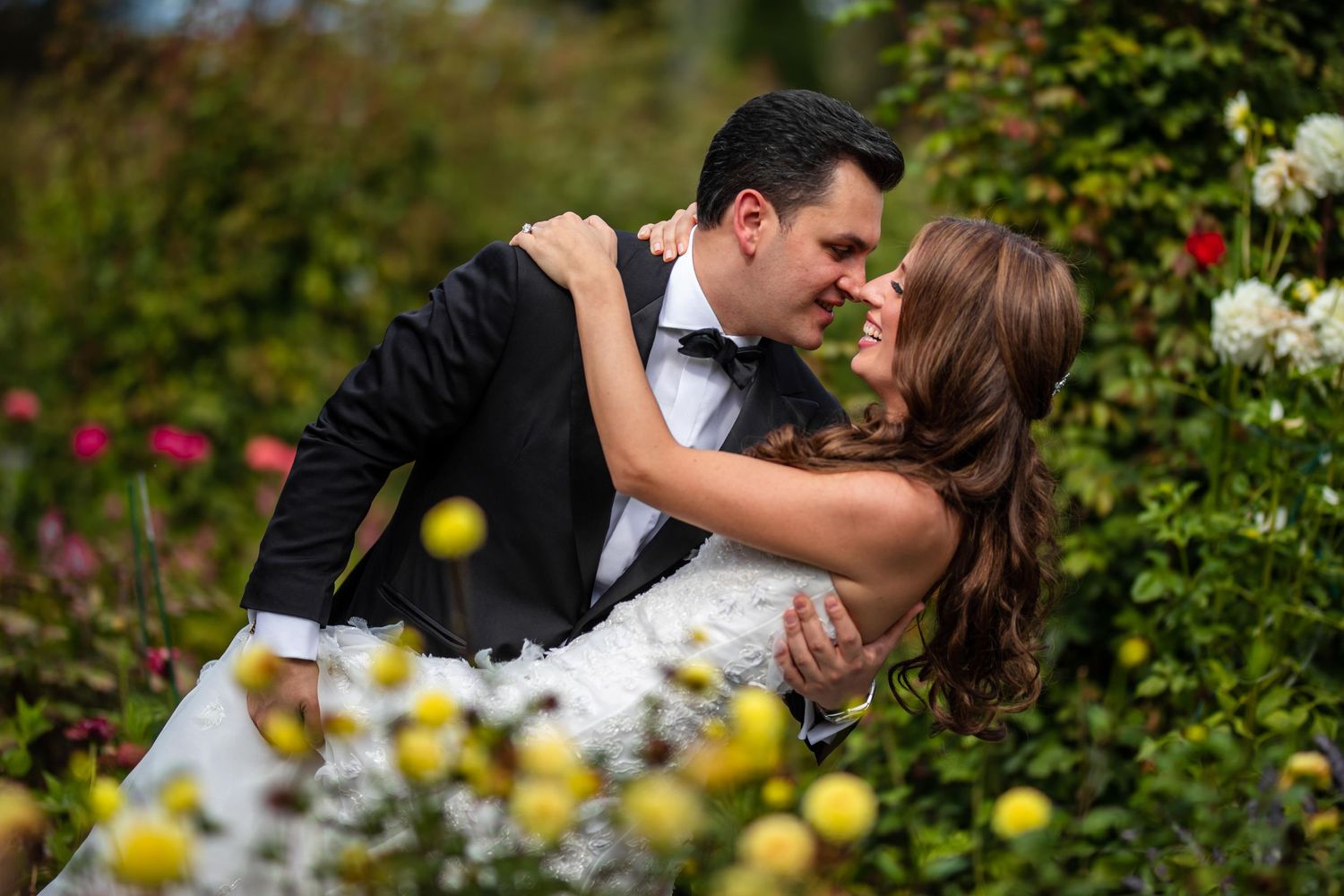 Romantic wedding couple embraces in a lush garden setting with blooming flowers and natural light.