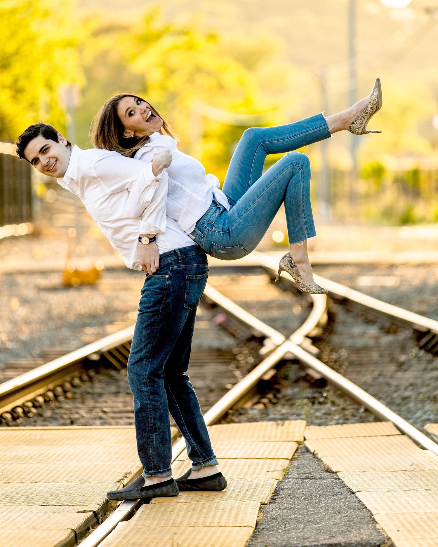 Playful couple posing on railroad tracks with vibrant yellow foliage in the background.