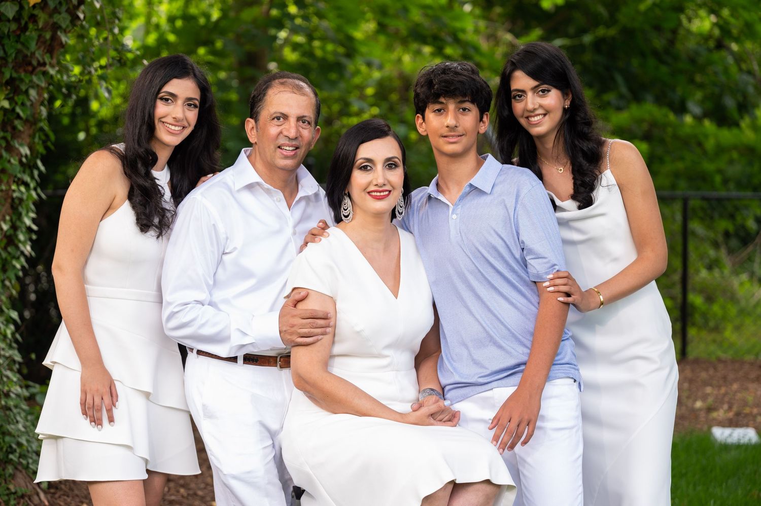 Family group wearing coordinated white and blue outfits in outdoor garden setting.