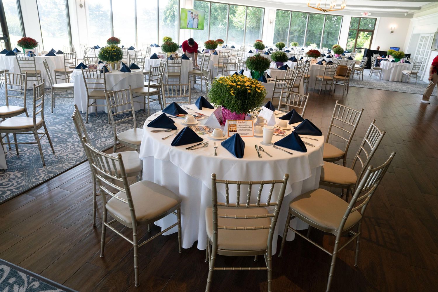 Elegant banquet hall with round tables set with white linens and blue napkins for a formal event.