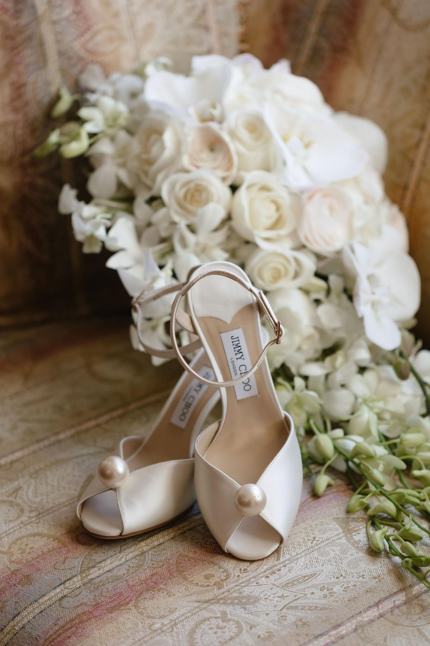 Elegant white bridal shoes displayed with white floral arrangements on a vintage surface.