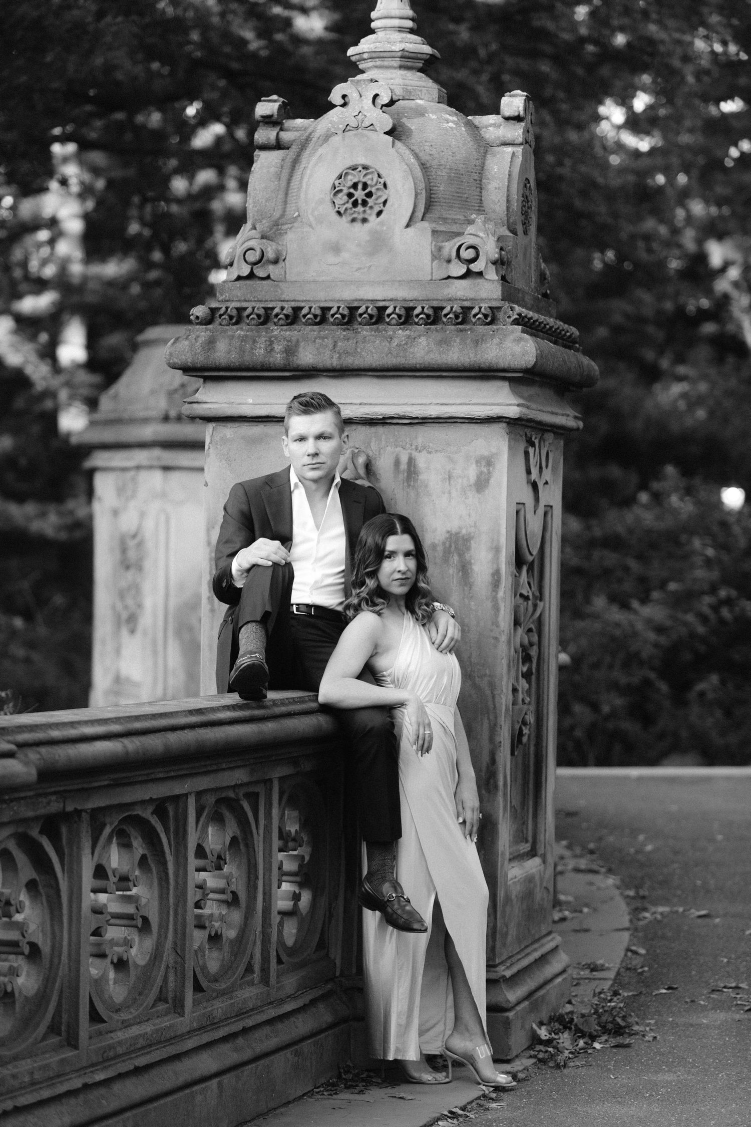A couple poses together on an ornate stone bridge in black and white photography.