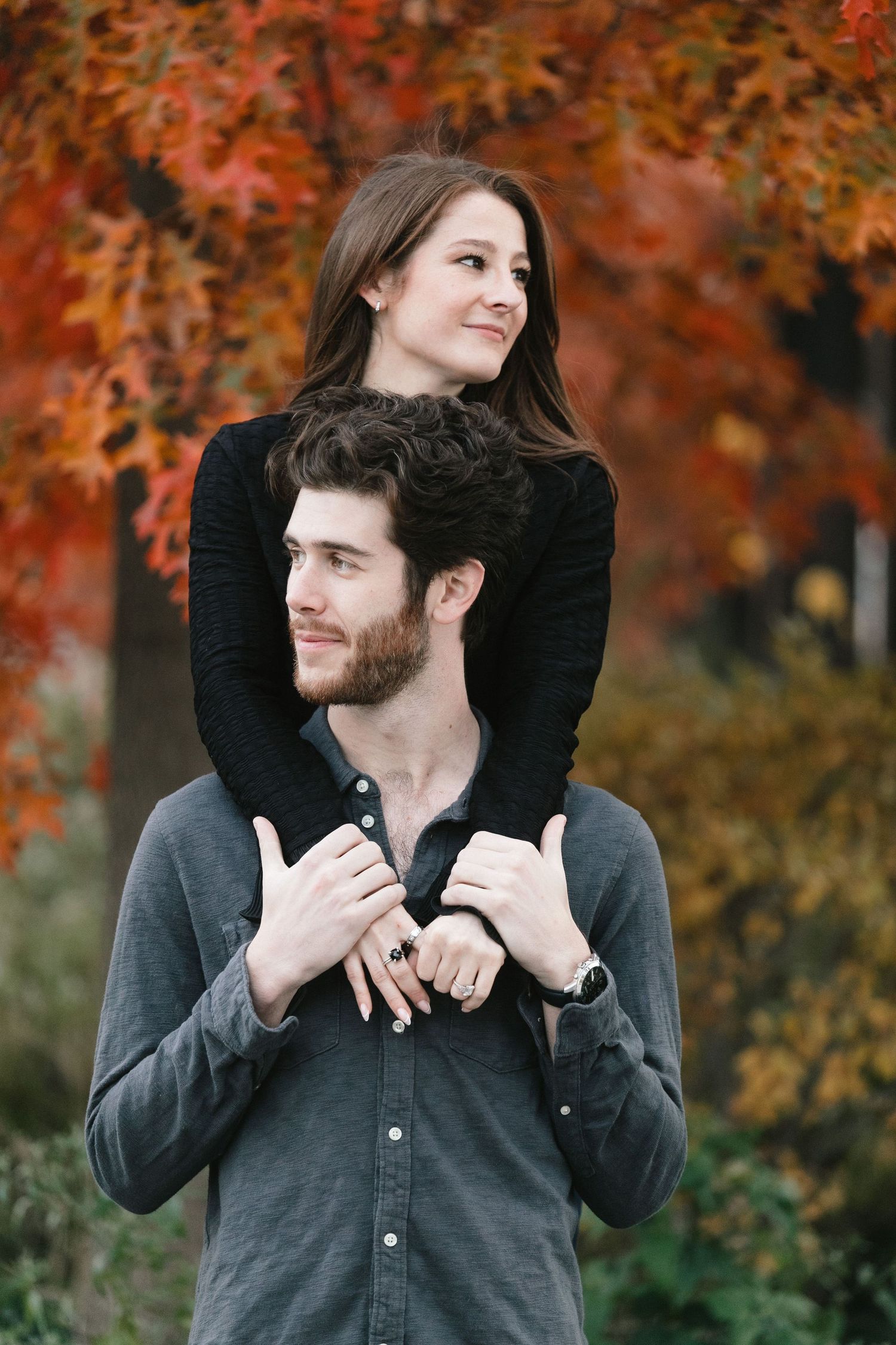 Autumn portrait of couple with vibrant orange fall foliage in background.