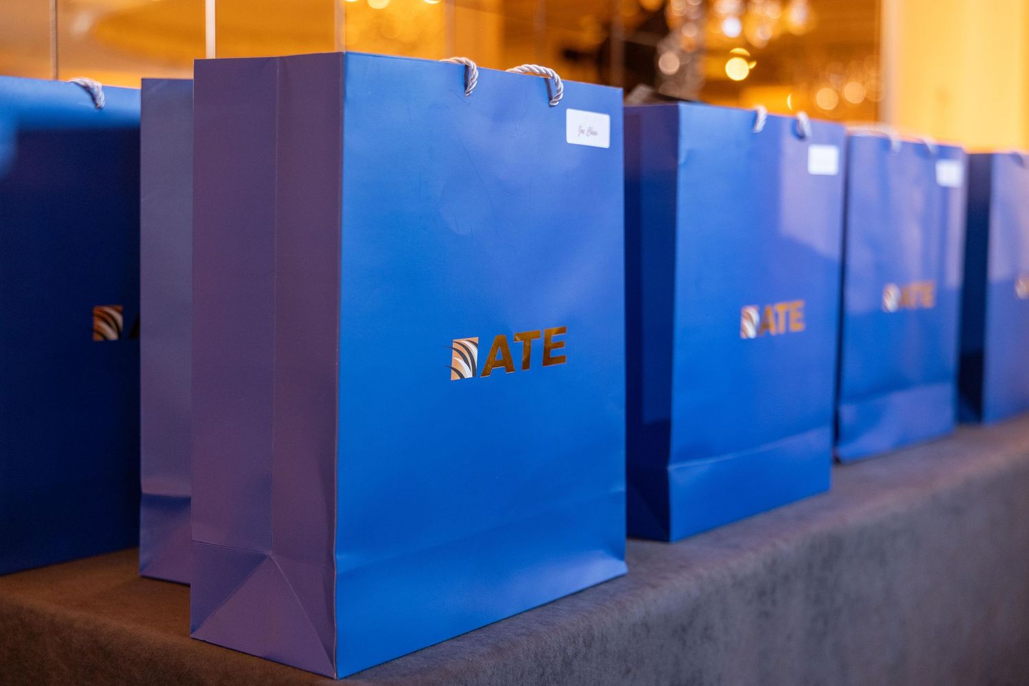 Blue ATE branded gift bags displayed in a row on a table at a corporate event.