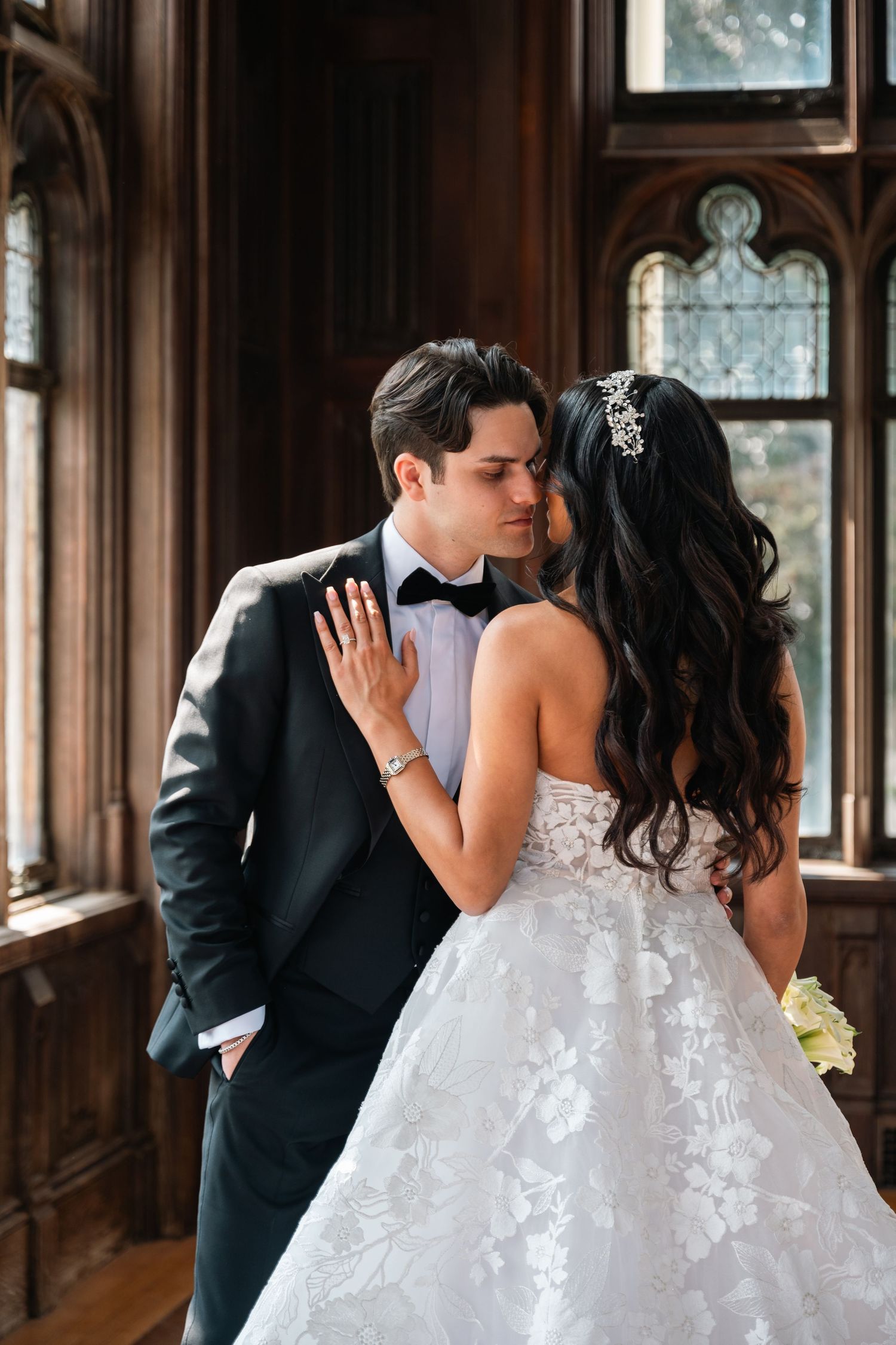 Romantic moment captured between couple in ornate wood-paneled room with gothic windows.