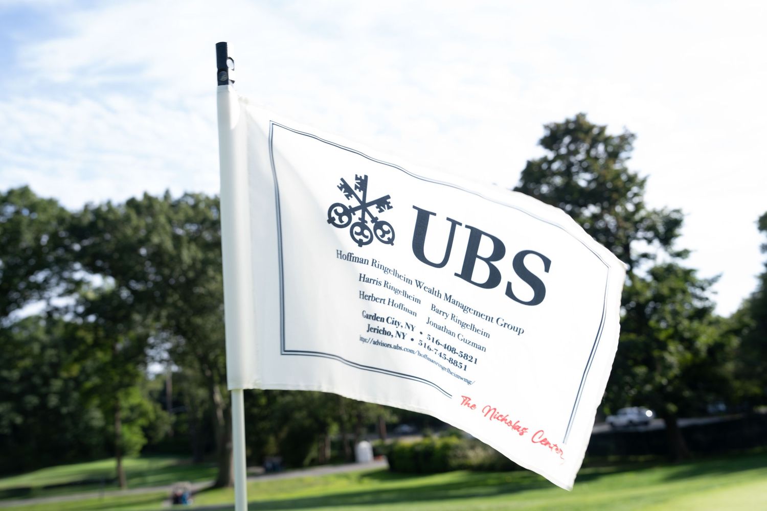 UBS Sullivan Wealth Management Group branded white golf flag on a sunny green course.