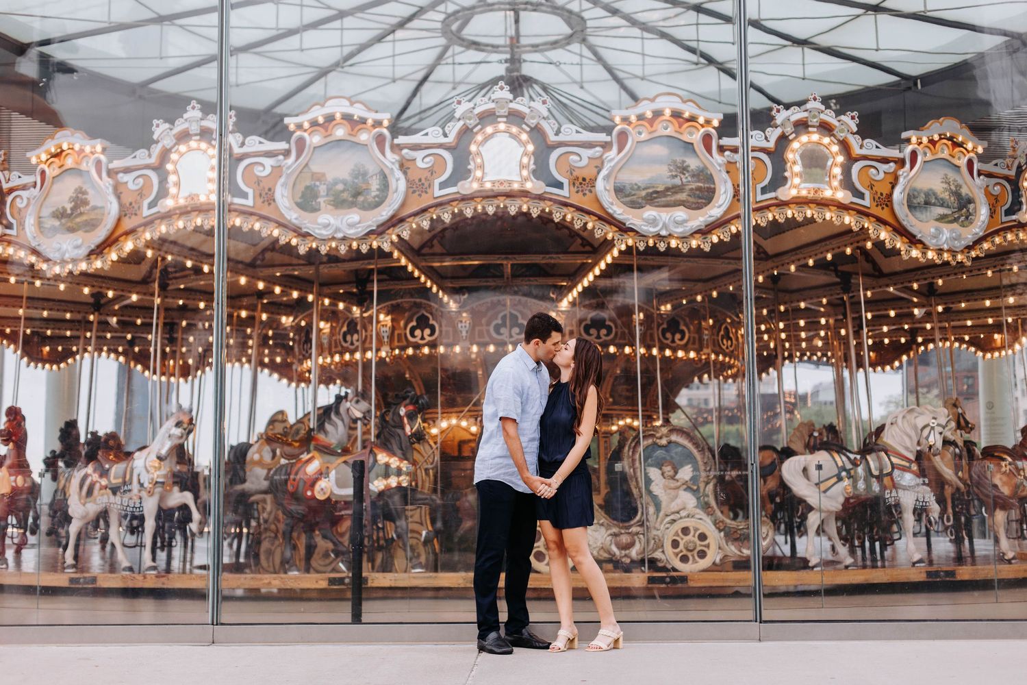 A couple shares a tender moment in front of an illuminated vintage carousel.