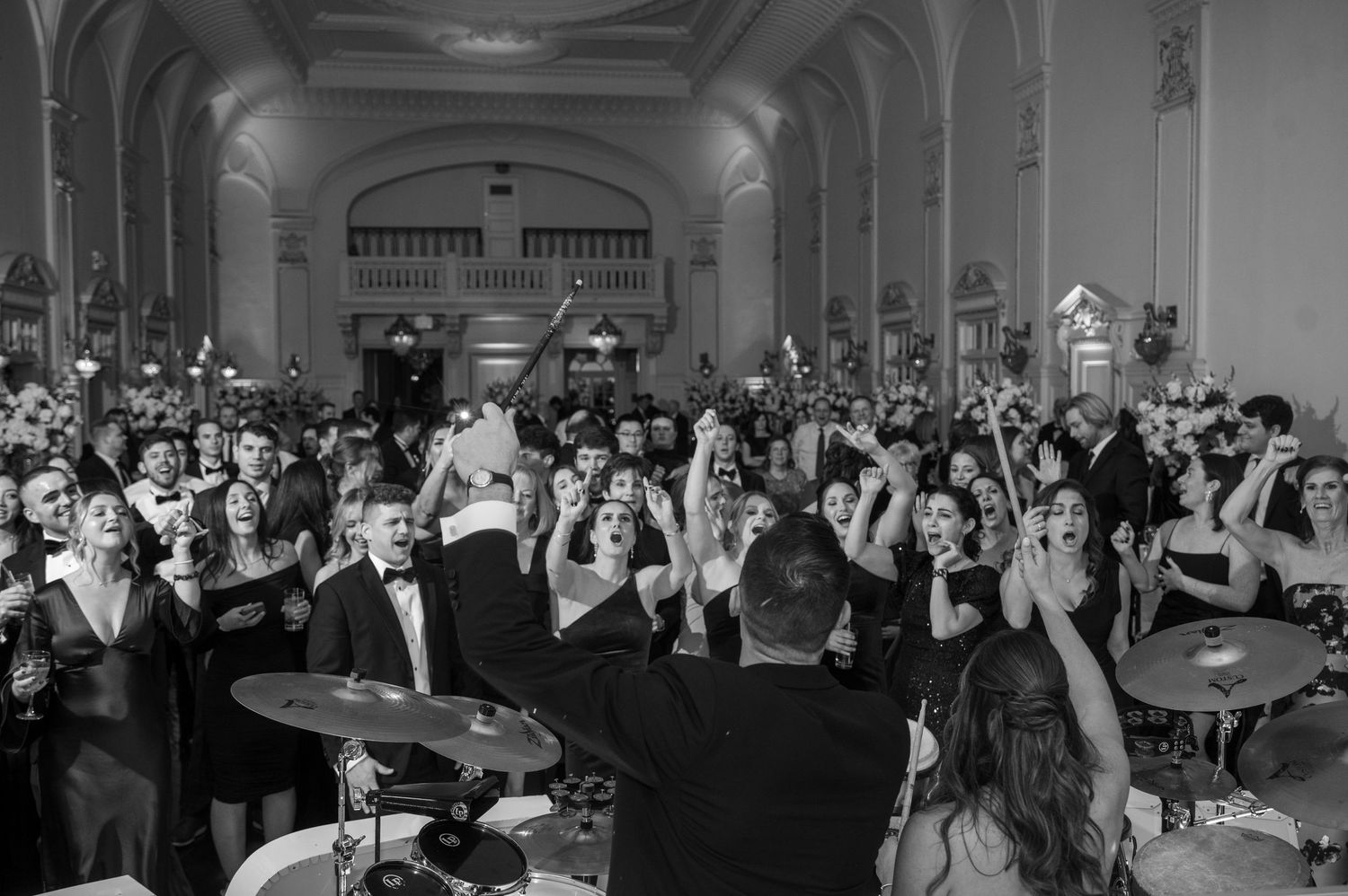 Black and white photo of a crowded dance floor at a wedding reception with a drummer in the foreground.