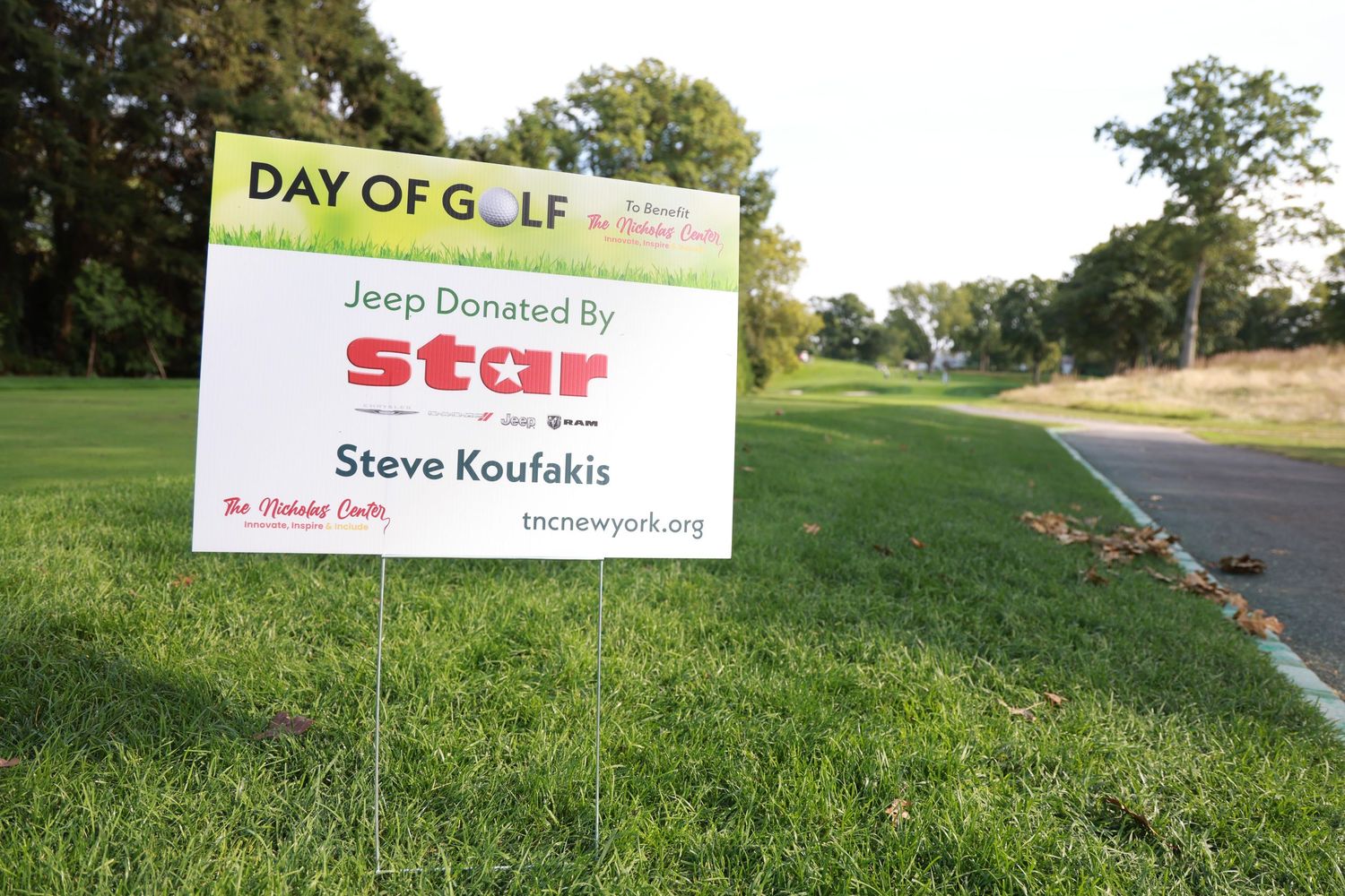 Day of Golf sign on green grass advertising a Jeep donated by Star, sponsored by Steve Koufakis at a charity golf event.