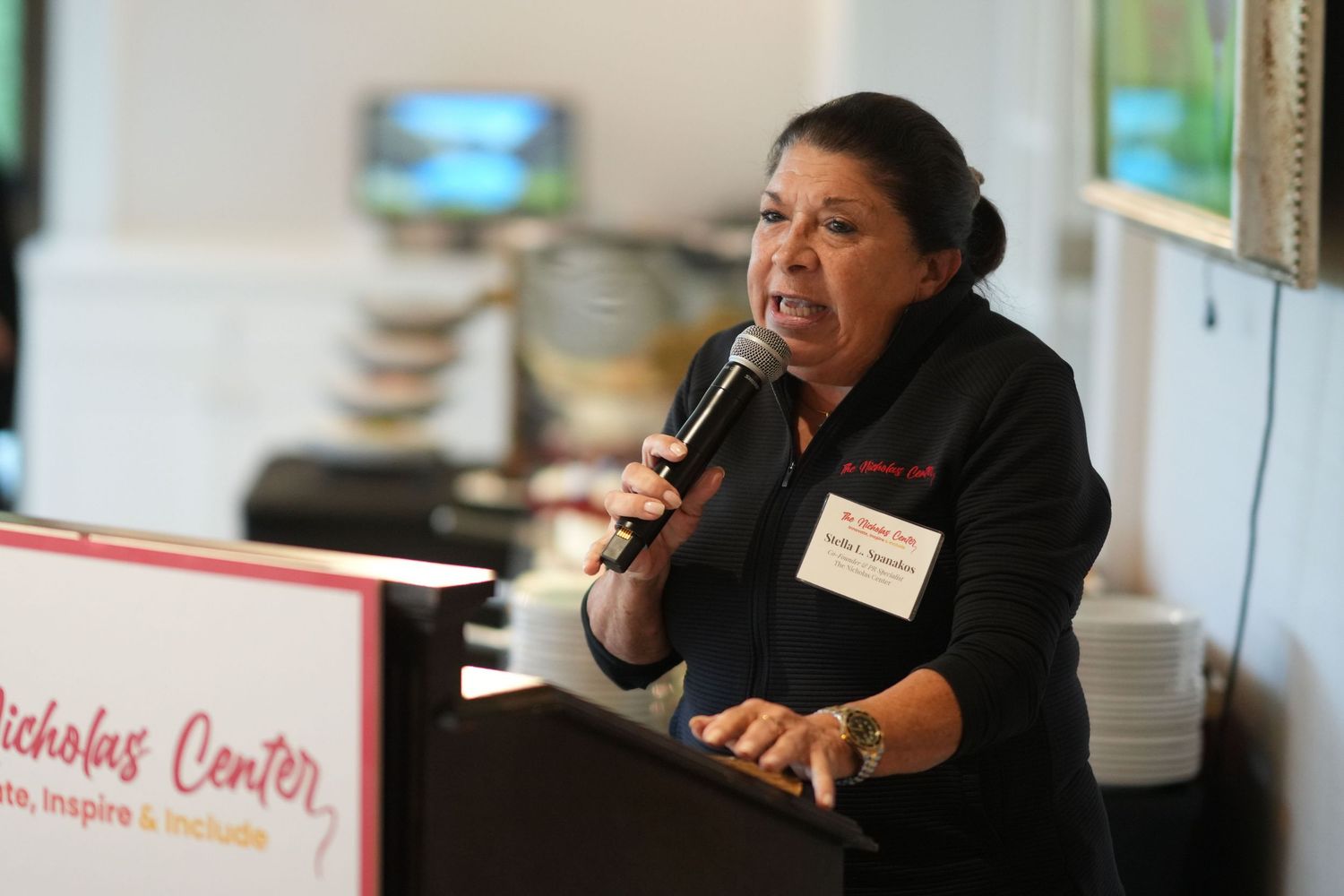 Woman speaking at a podium with a microphone at a Nicholas Center fundraising event.