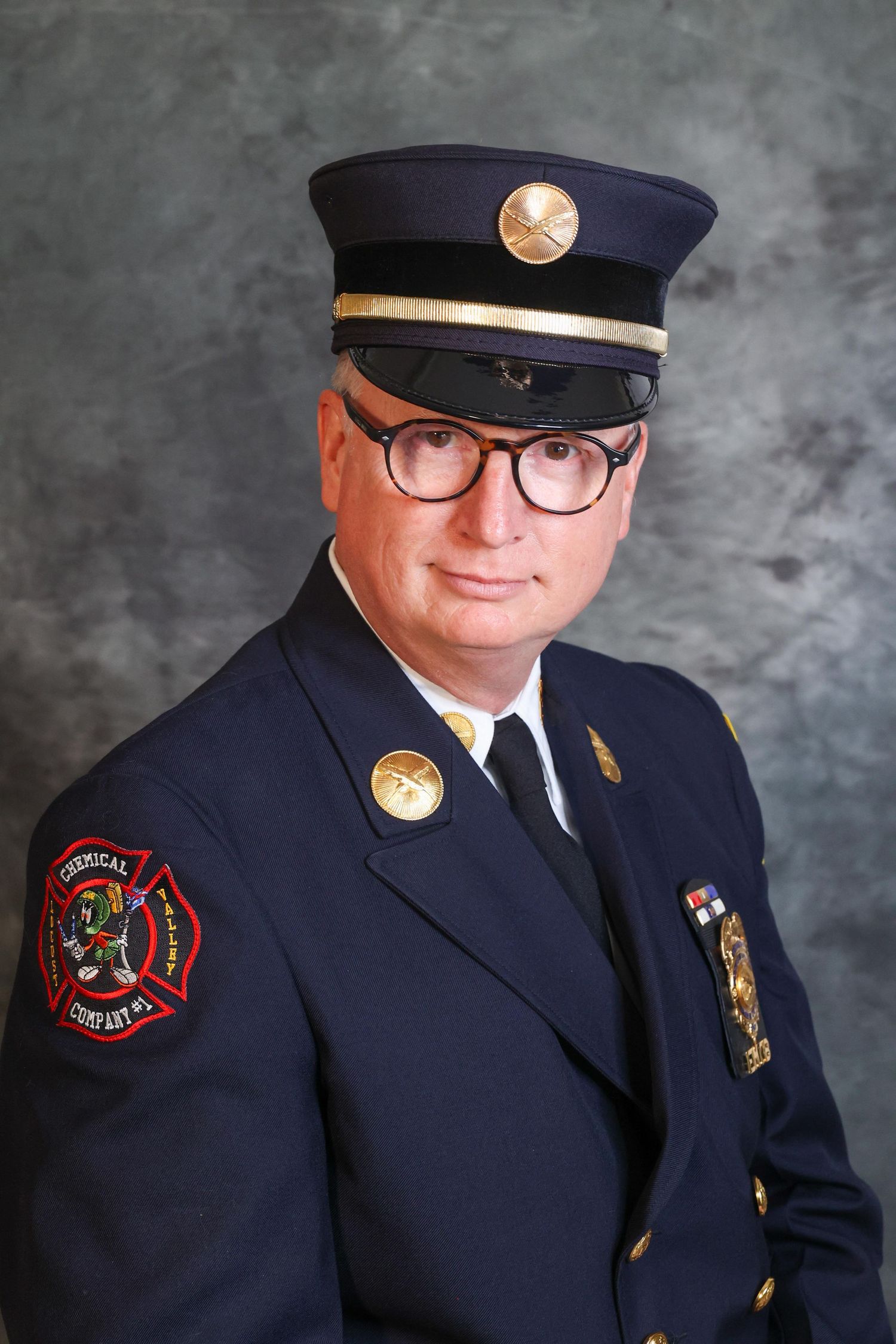 Firefighter in formal dress uniform with badges and cap poses for official portrait.