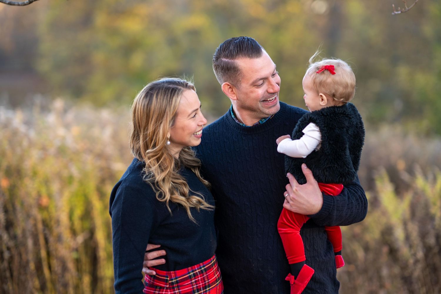 Family wearing coordinated red and black outfits poses together during an autumn outdoor photoshoot.
