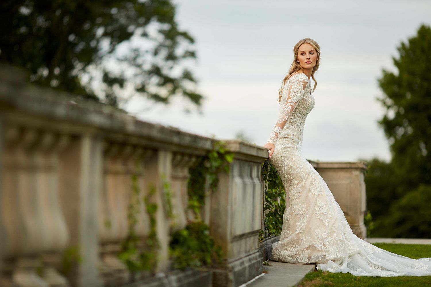 Elegant wedding party posing on stone balcony with classical architecture and greenery.