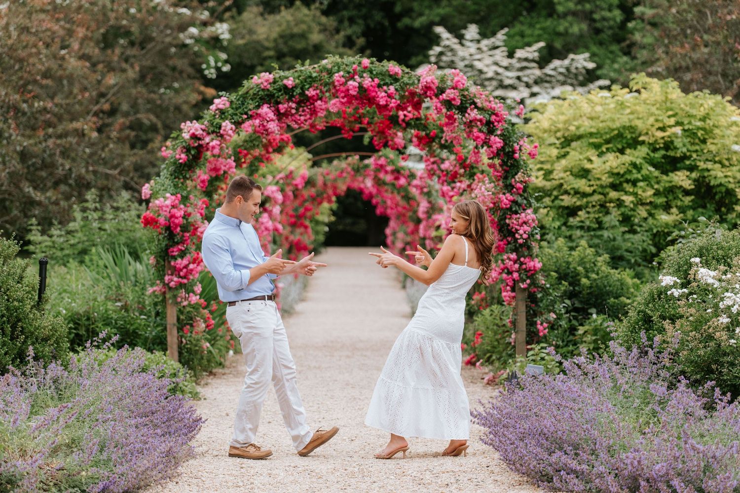 A couple walks through a garden path lined with vibrant pink flowers and purple lavender.