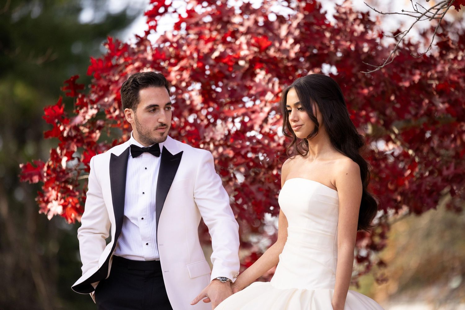 Romantic wedding portraits against vibrant red autumn foliage in an outdoor setting.
