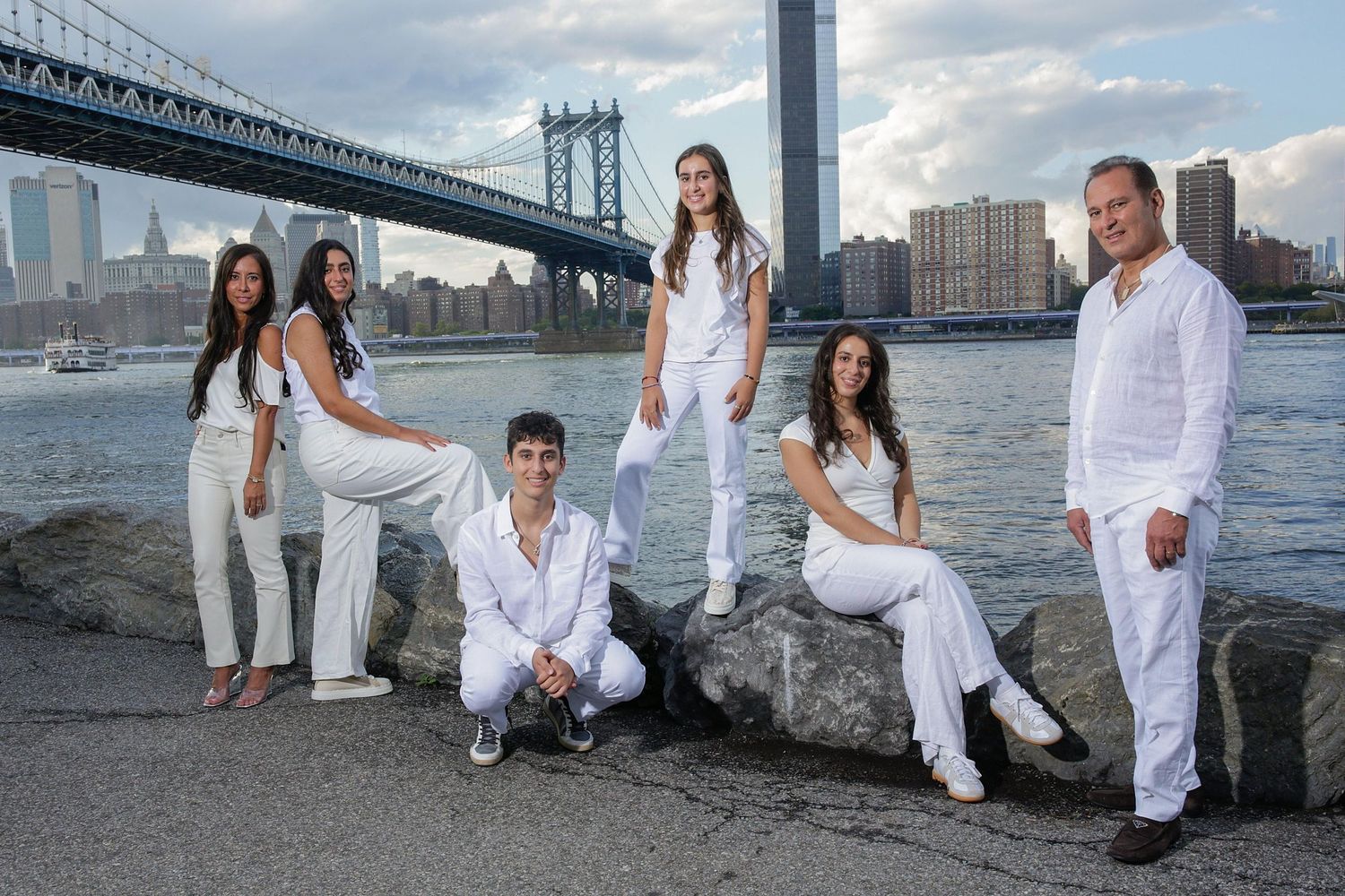 A group in white outfits poses along the waterfront with the New York City skyline visible in the background.