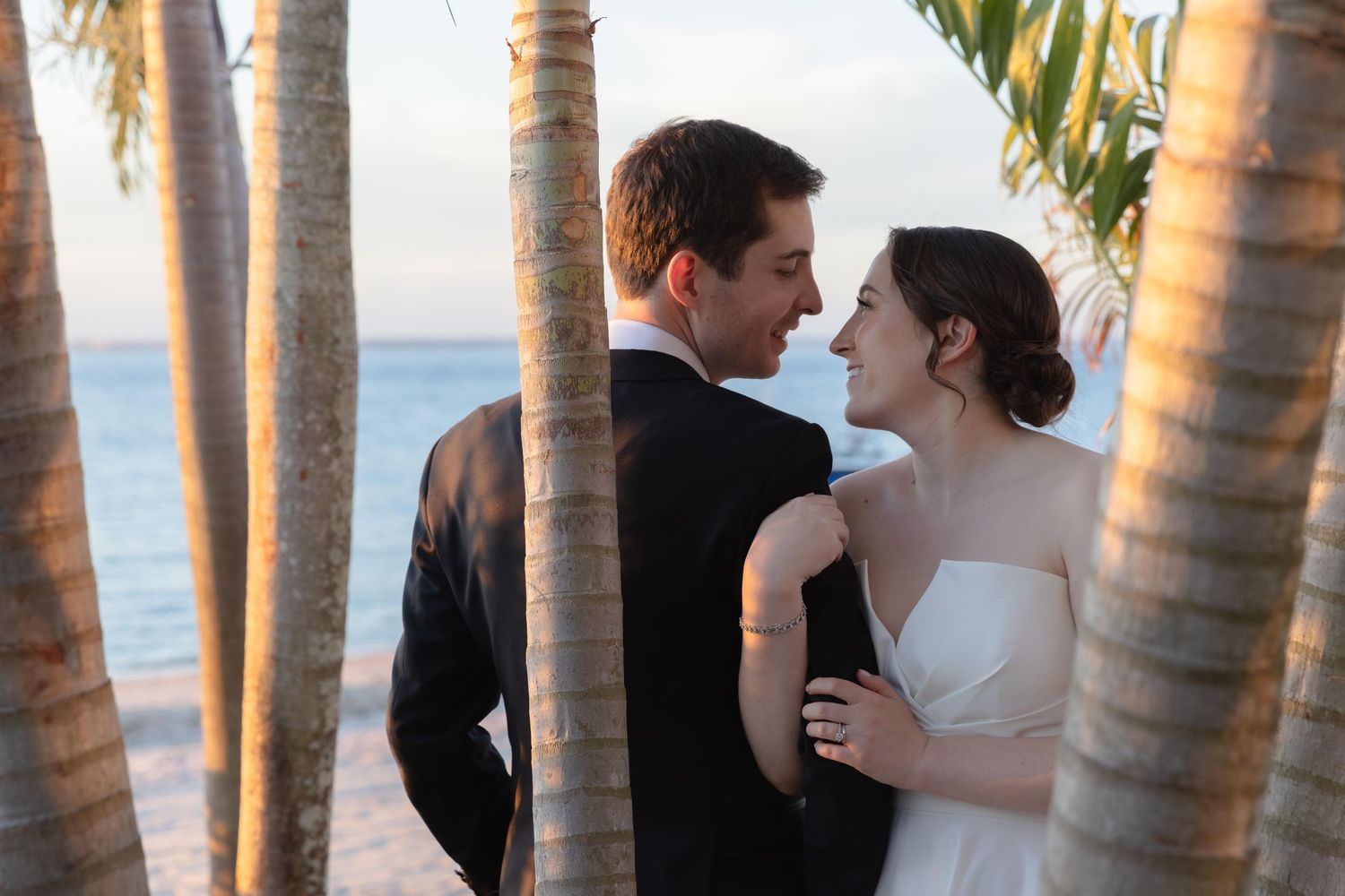 A romantic moment between newlyweds among palm trees at sunset by the ocean.