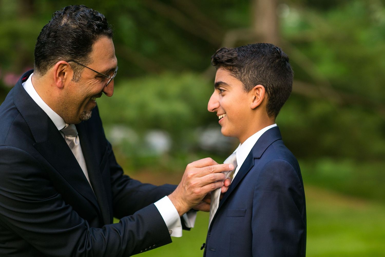 A formal ceremony preparation moment with men in black suits adjusting attire outdoors.