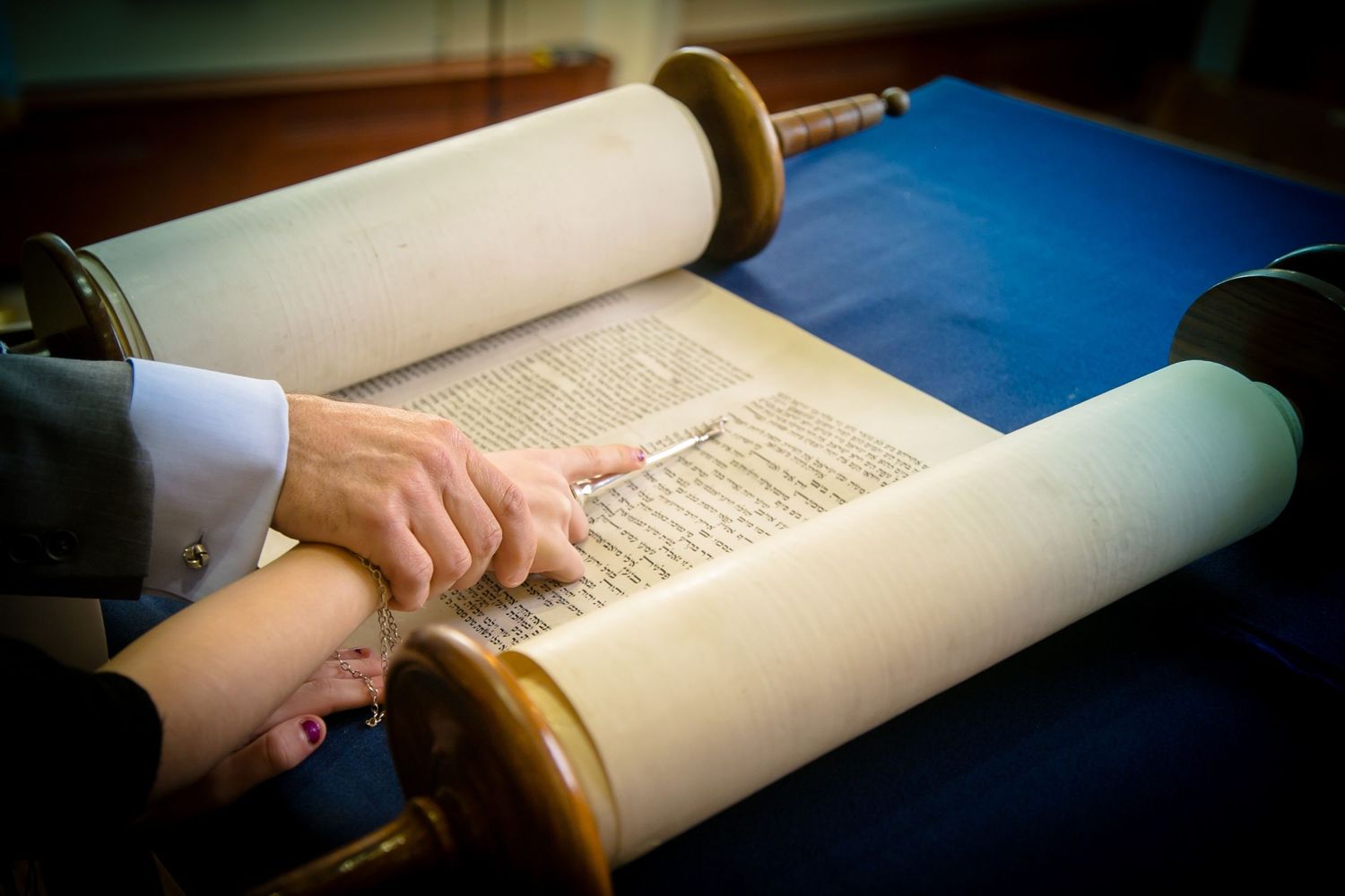 Ancient Torah scroll being read on blue cloth during religious ceremony.
