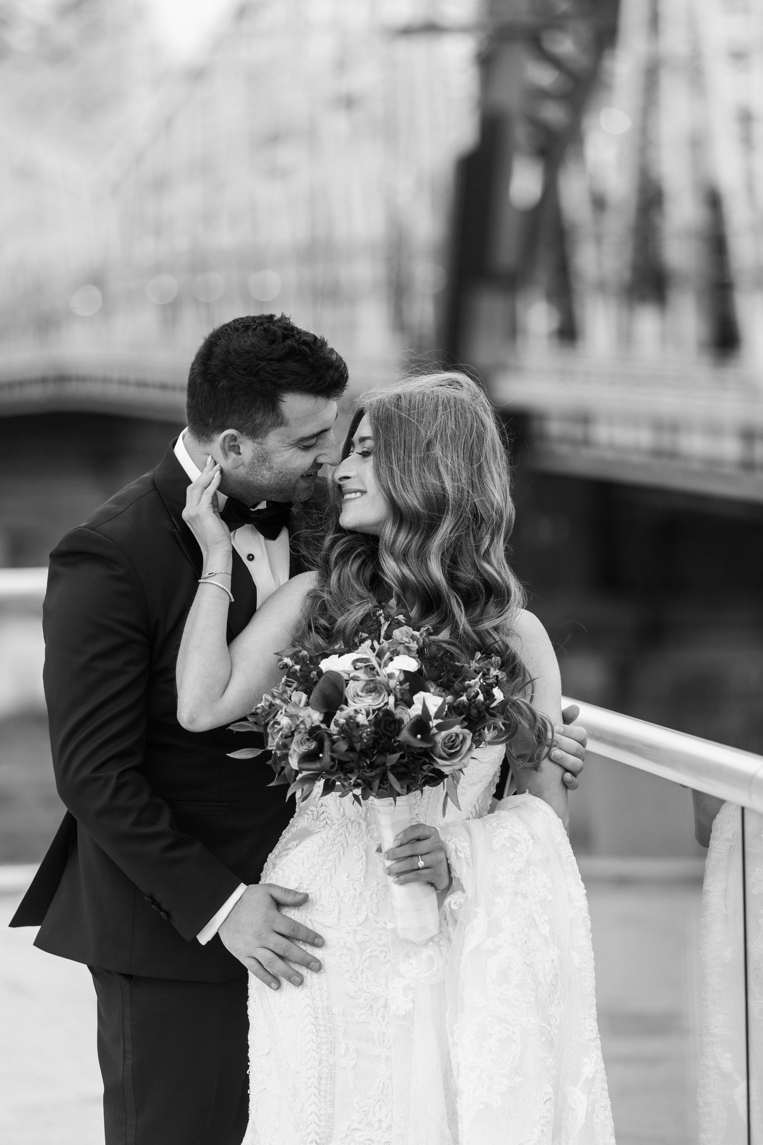 A romantic black and white portrait of newlyweds sharing an intimate moment on a bridge.