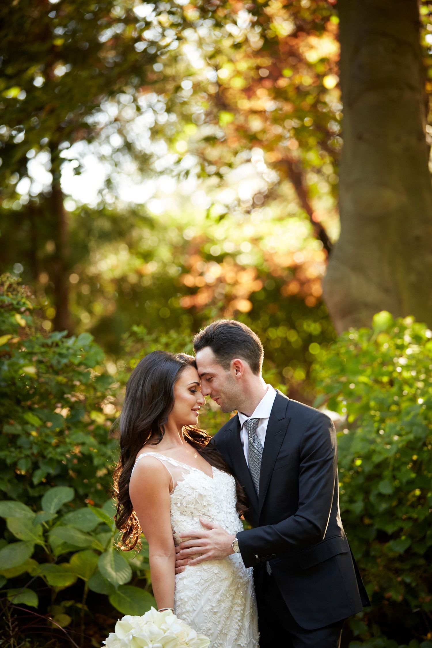 A romantic moment between newlyweds in a sunlit garden with golden bokeh lighting effects.