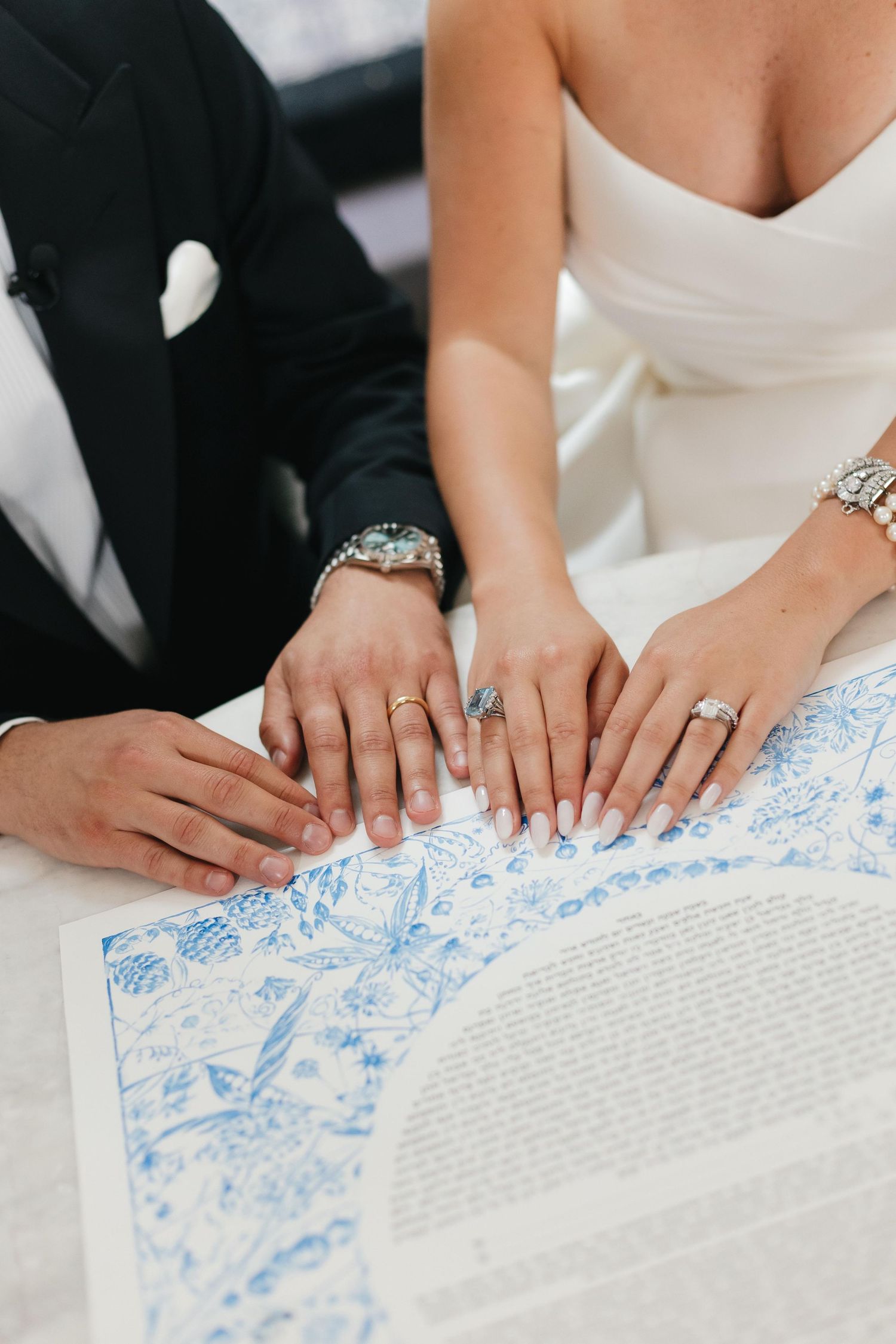 Close-up of couple's hands signing a decorative wedding document with blue details.