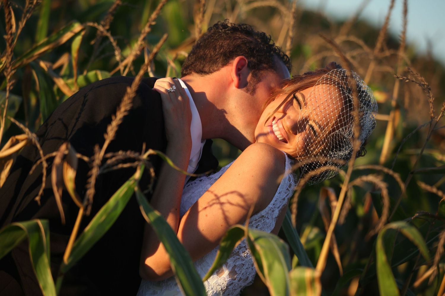 Intimate wedding moment captured in golden sunlight among cornfield at sunset.