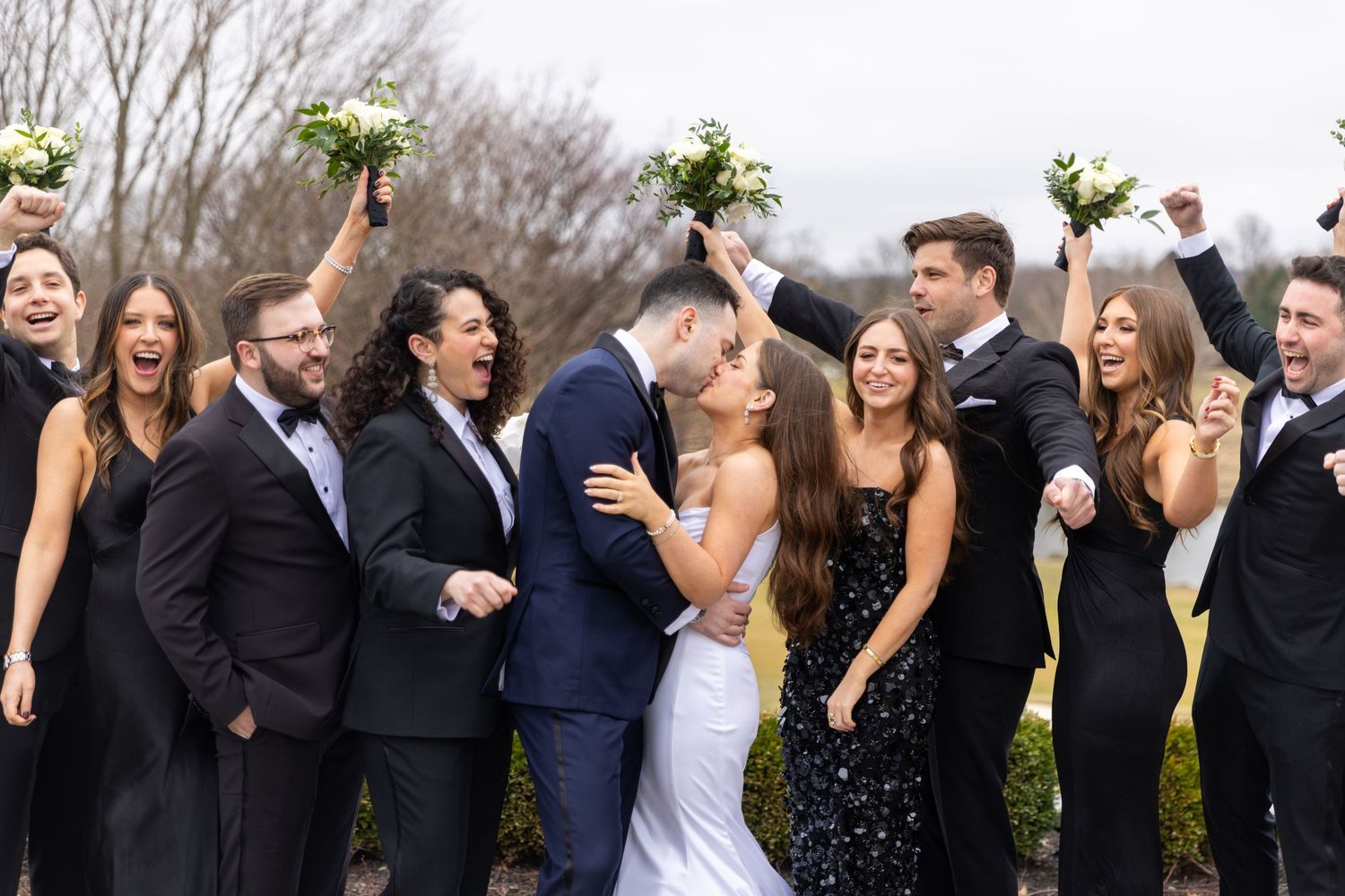 Wedding party members laugh and celebrate together wearing formal black attire.