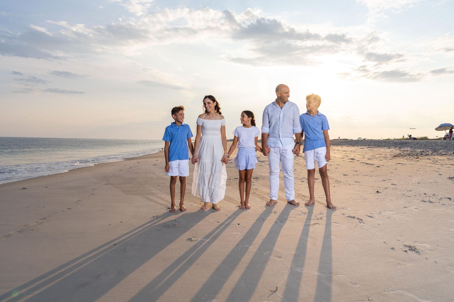 Group walking along a sandy beach at sunset casting long shadows on the shoreline.