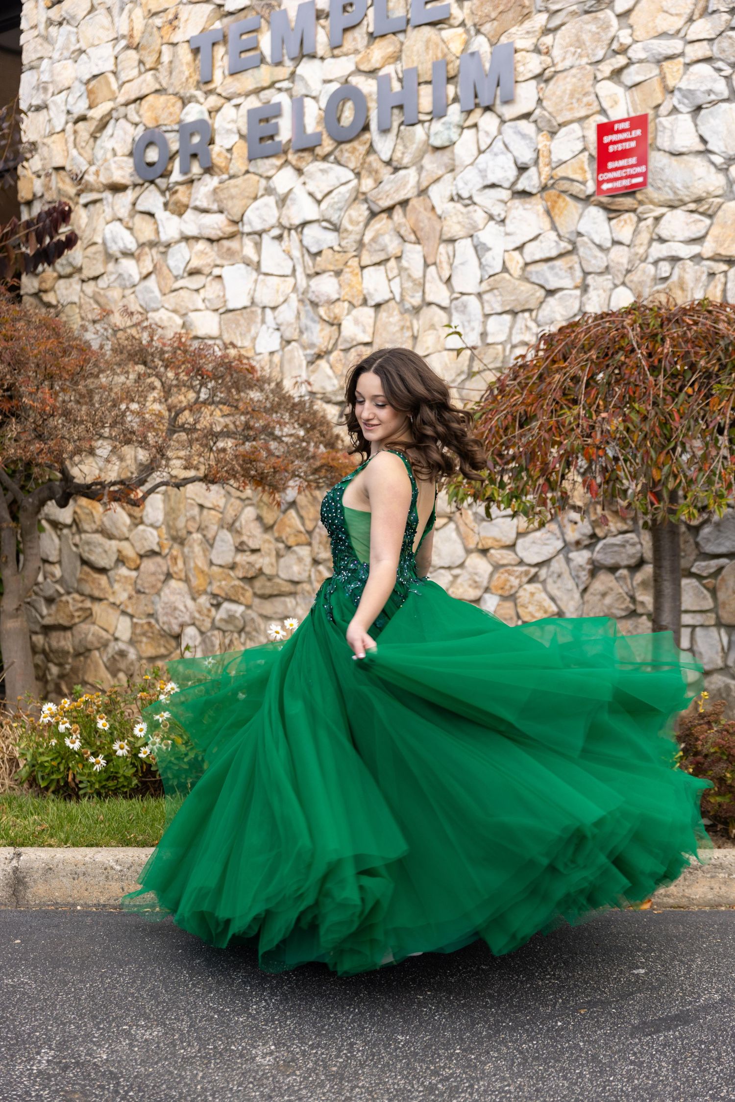 Young woman twirling in an emerald green ball gown outside Temple Or Elohim, showcasing the dress's full tulle skirt.