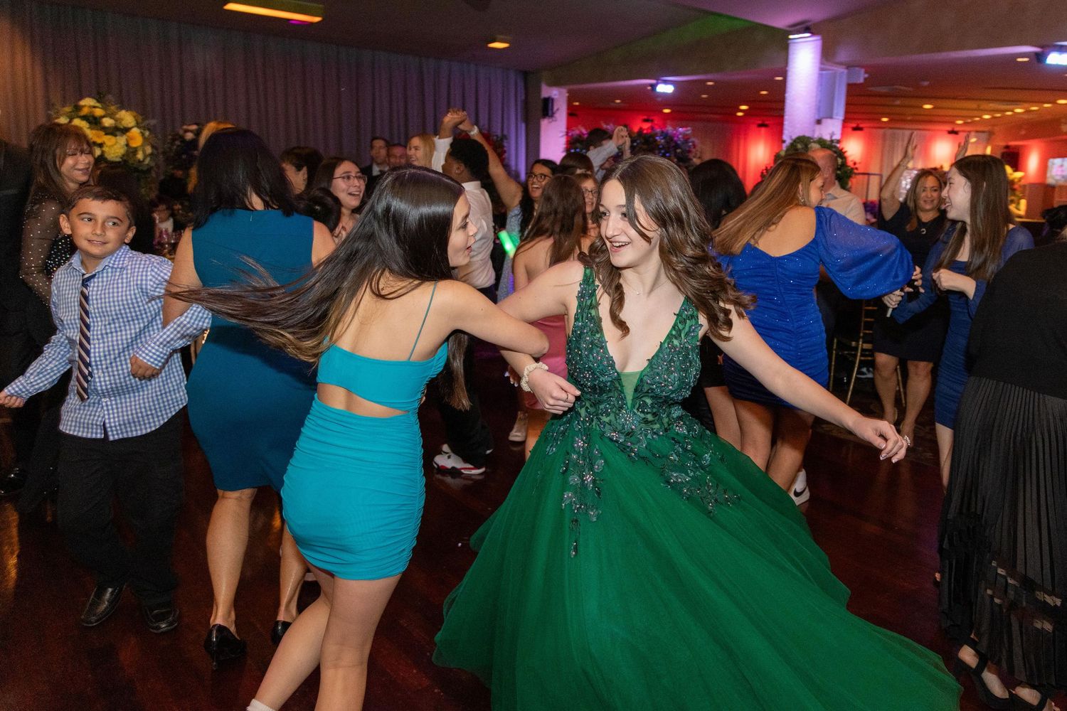 Party guests dancing and celebrating on a colorfully lit dance floor at an event.