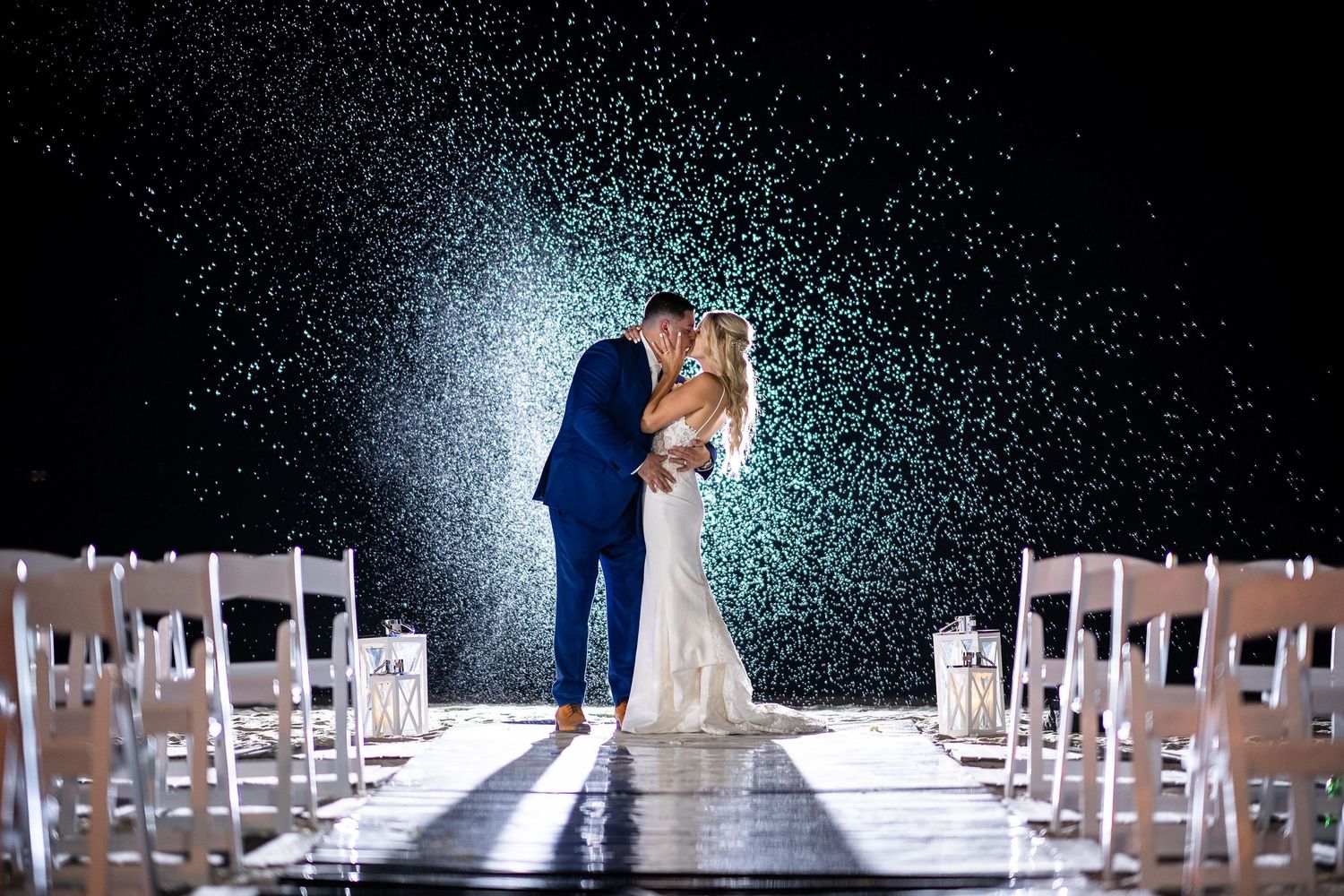 A couple shares an intimate moment in falling snow under dramatic lighting on their wedding aisle.