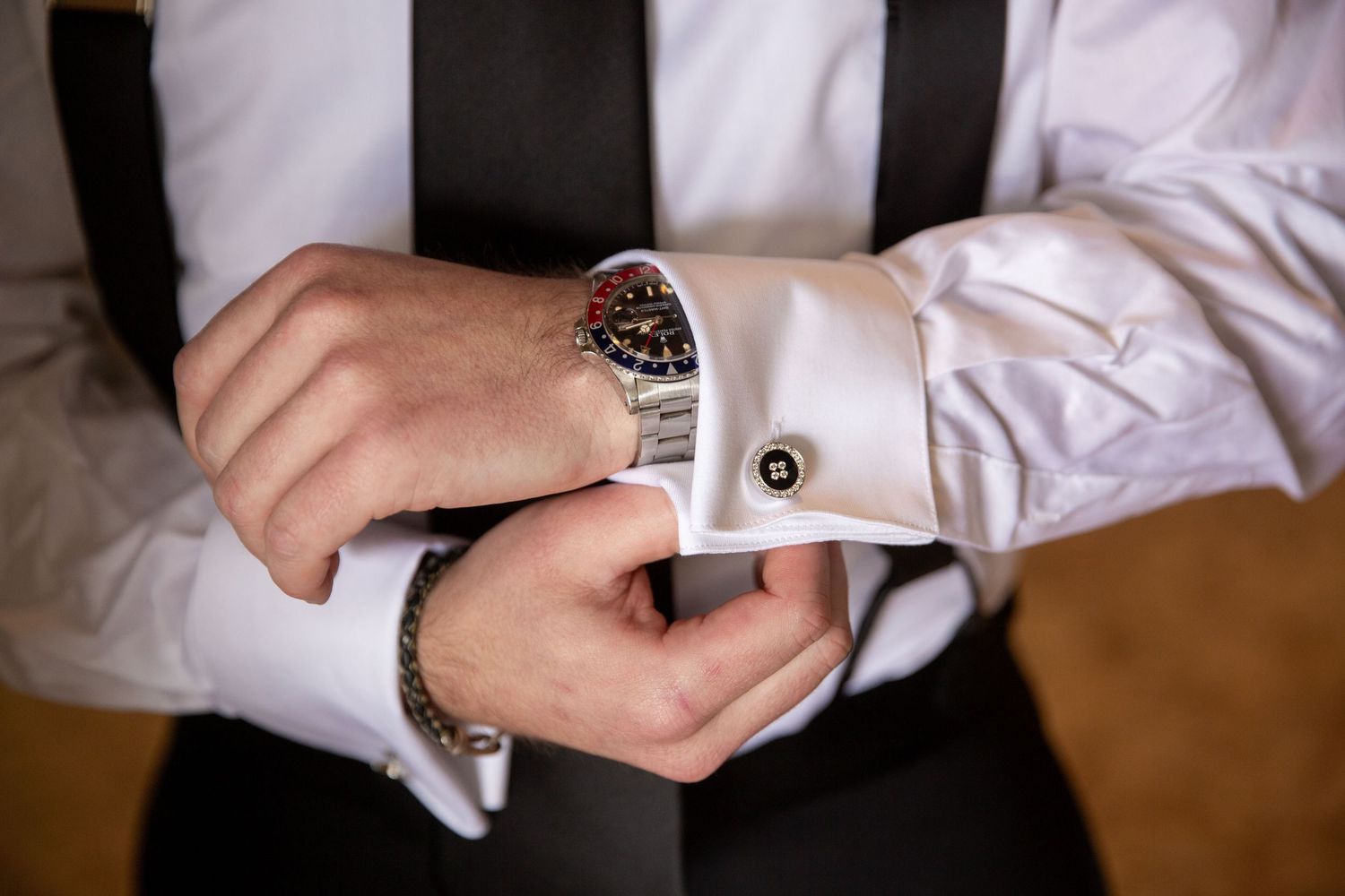 Groom adjusts cufflinks and watch while getting ready.