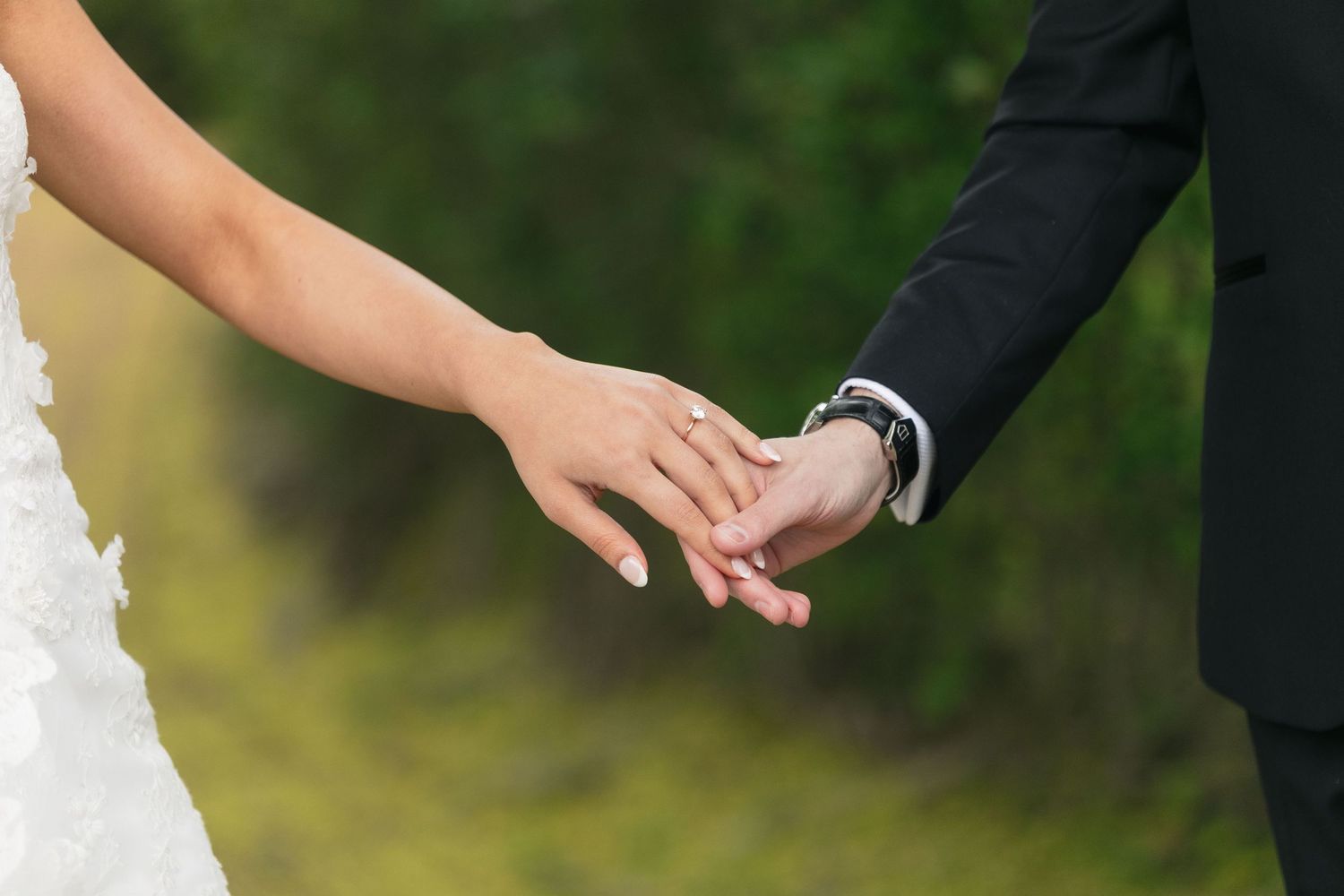 A couple holds hands tenderly during an outdoor wedding ceremony.