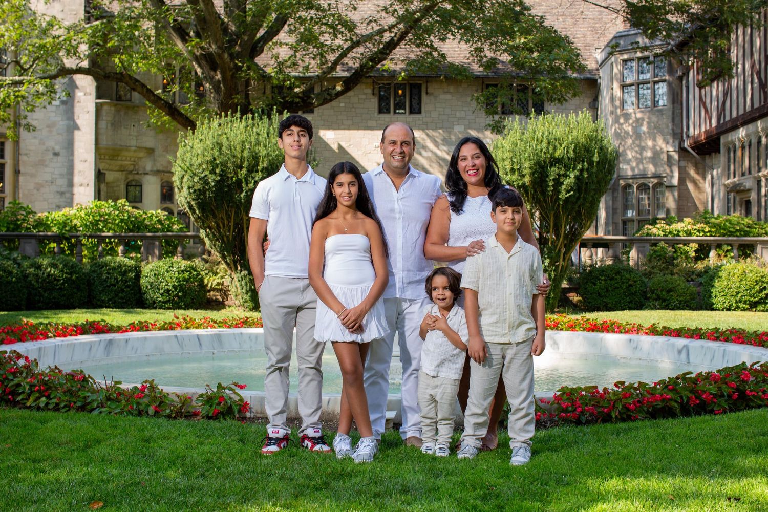 Group poses together in white and beige outfits for outdoor family portraits in a garden setting.