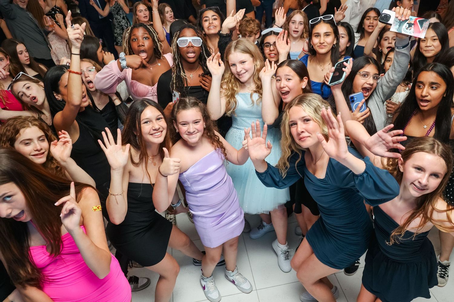 Large crowd of party guests dancing and celebrating with hands raised.