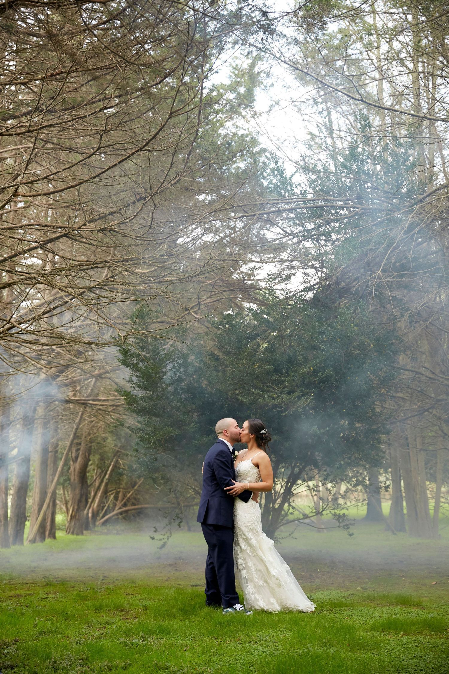 Newlyweds share an intimate moment in a misty forest setting.