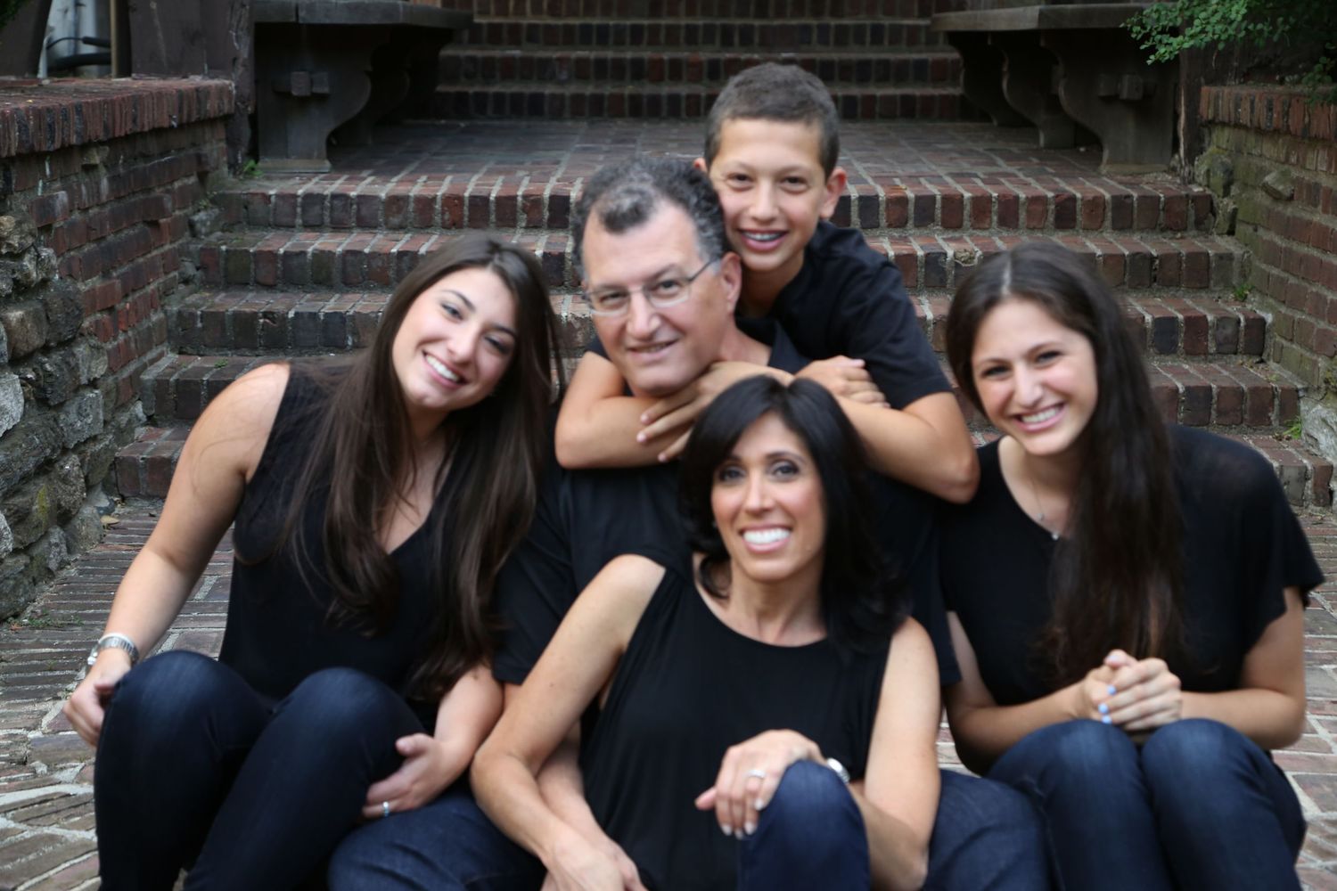 A group in black clothing poses together on brick steps during a casual outdoor photo session.