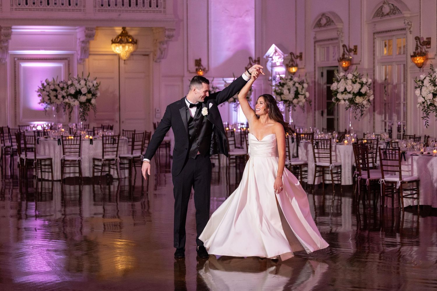 Elegant ballroom wedding reception with purple uplighting and romantic dance floor moments.