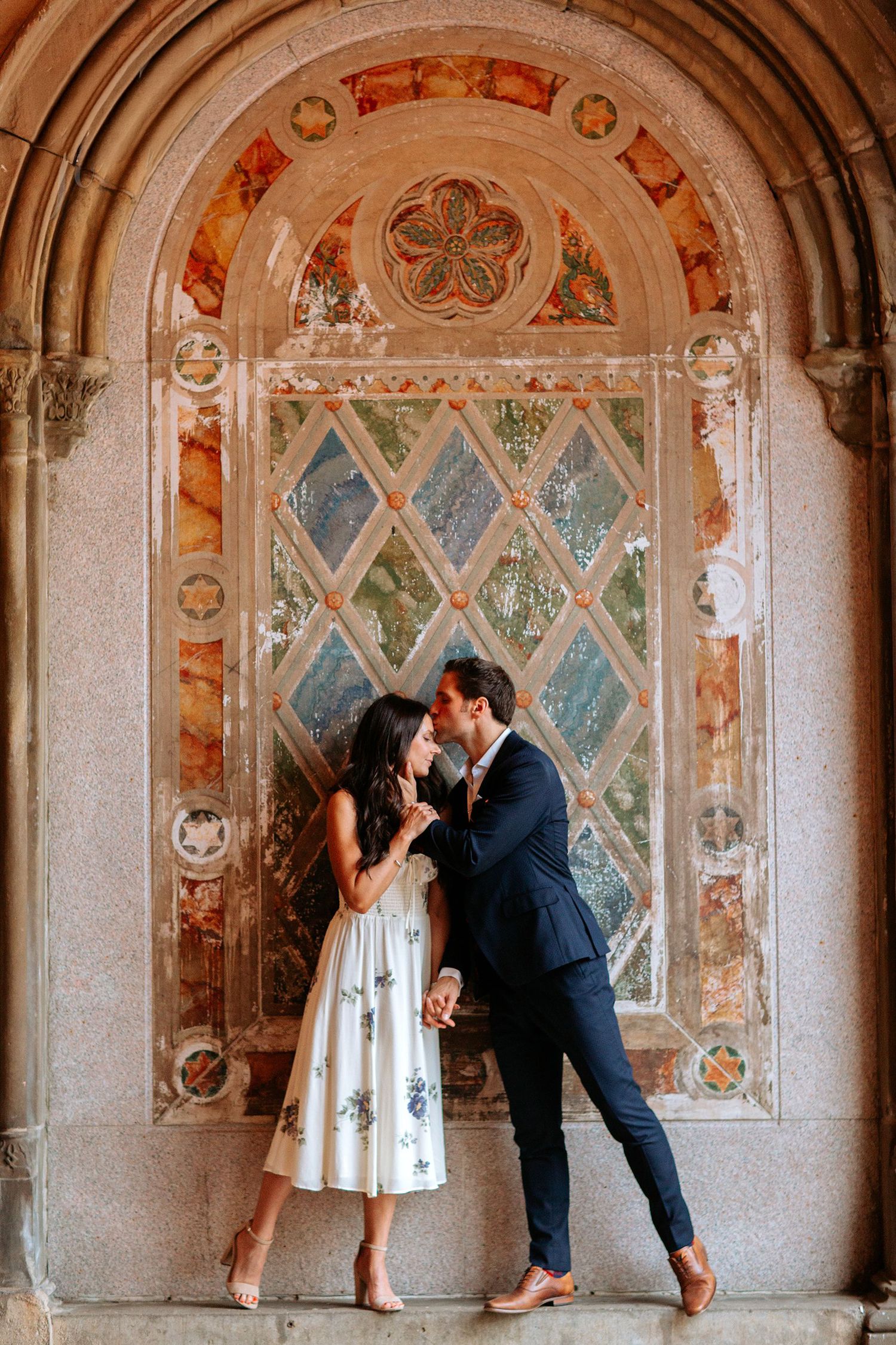 Couple shares romantic moment in front of ornate architectural doorway with stained glass details.
