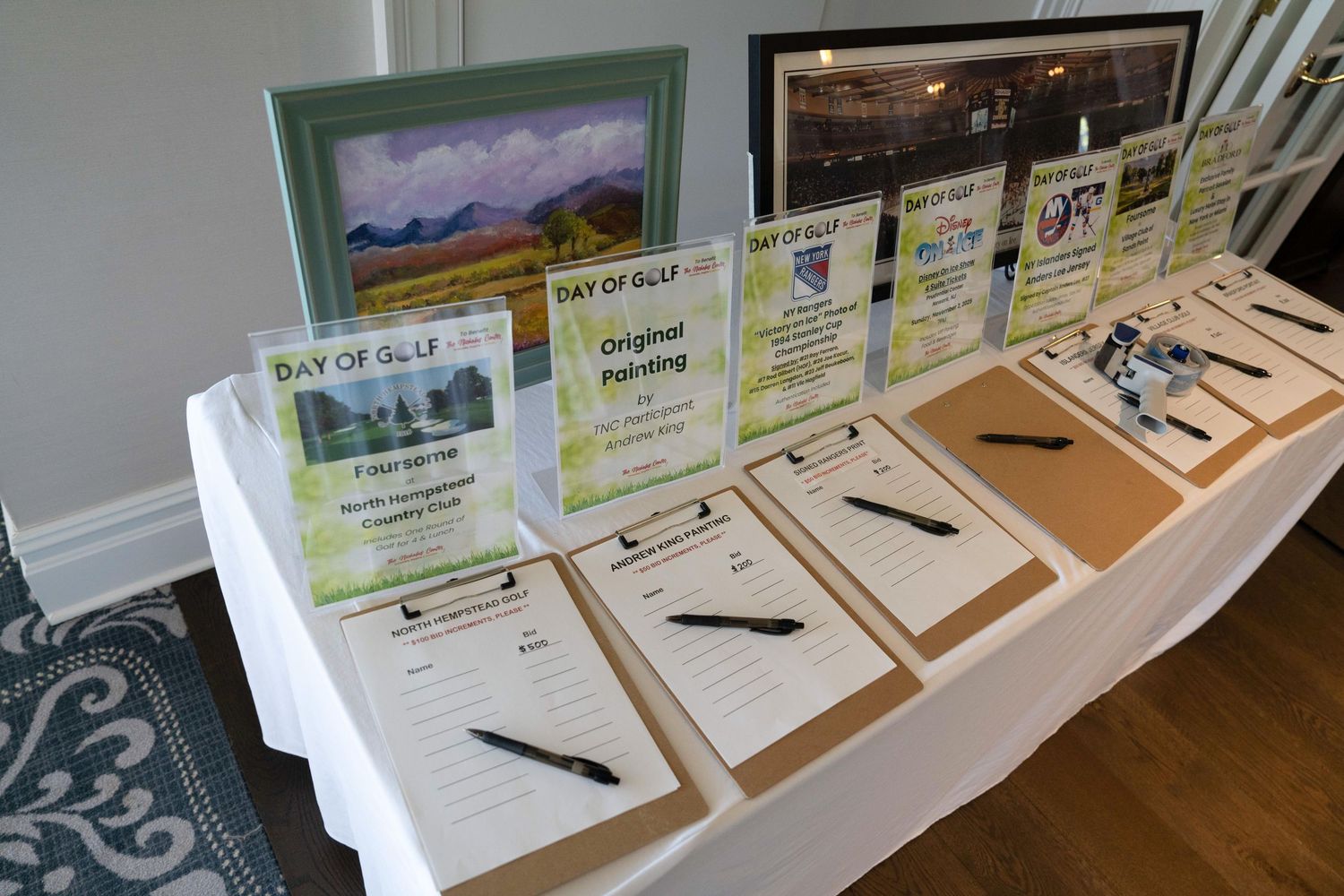 Silent auction bidding tables with clipboards and artwork displays at Day of Golf charity event.