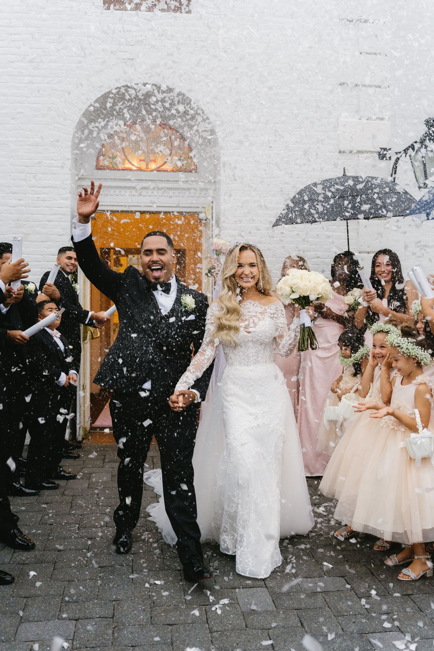 Bride and groom exit church ceremony in confetti shower, guests cheering in background.