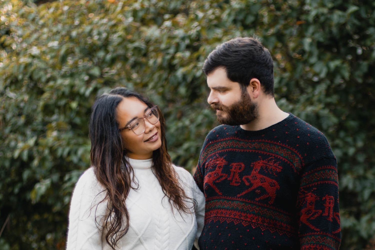 A couple wearing winter sweaters share tender moments together in a garden setting with autumn foliage.