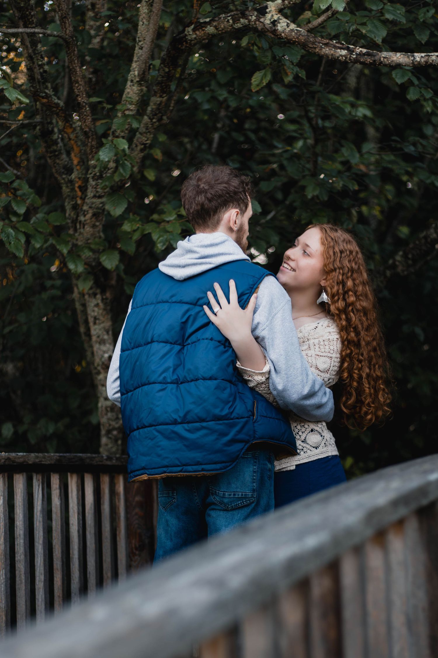A couple embraces on a wooden bridge surrounded by lush greenery during an outdoor session.