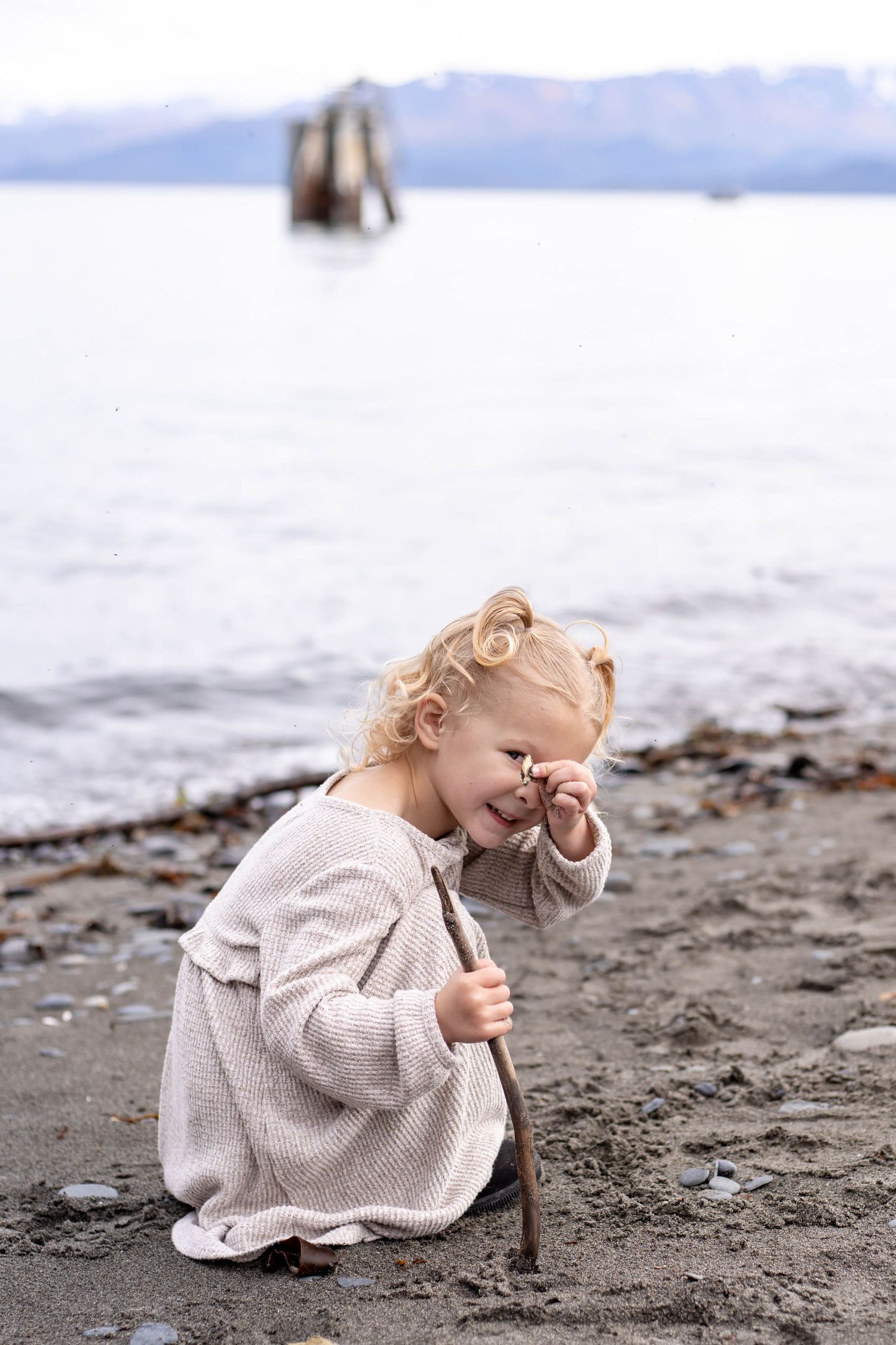 A sequence of images showing someone in a beige sweater sitting and playing in sand at the beach.