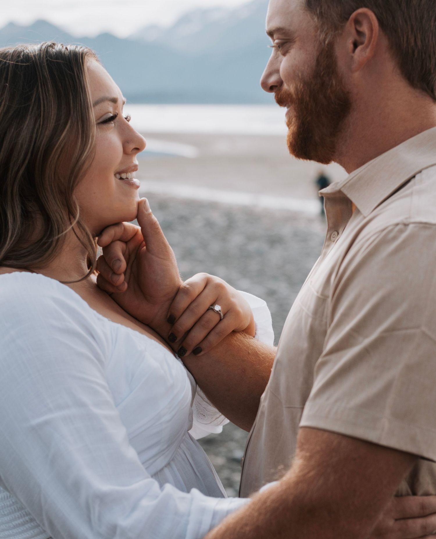 A romantic couple embraces on the beach during an overcast day.