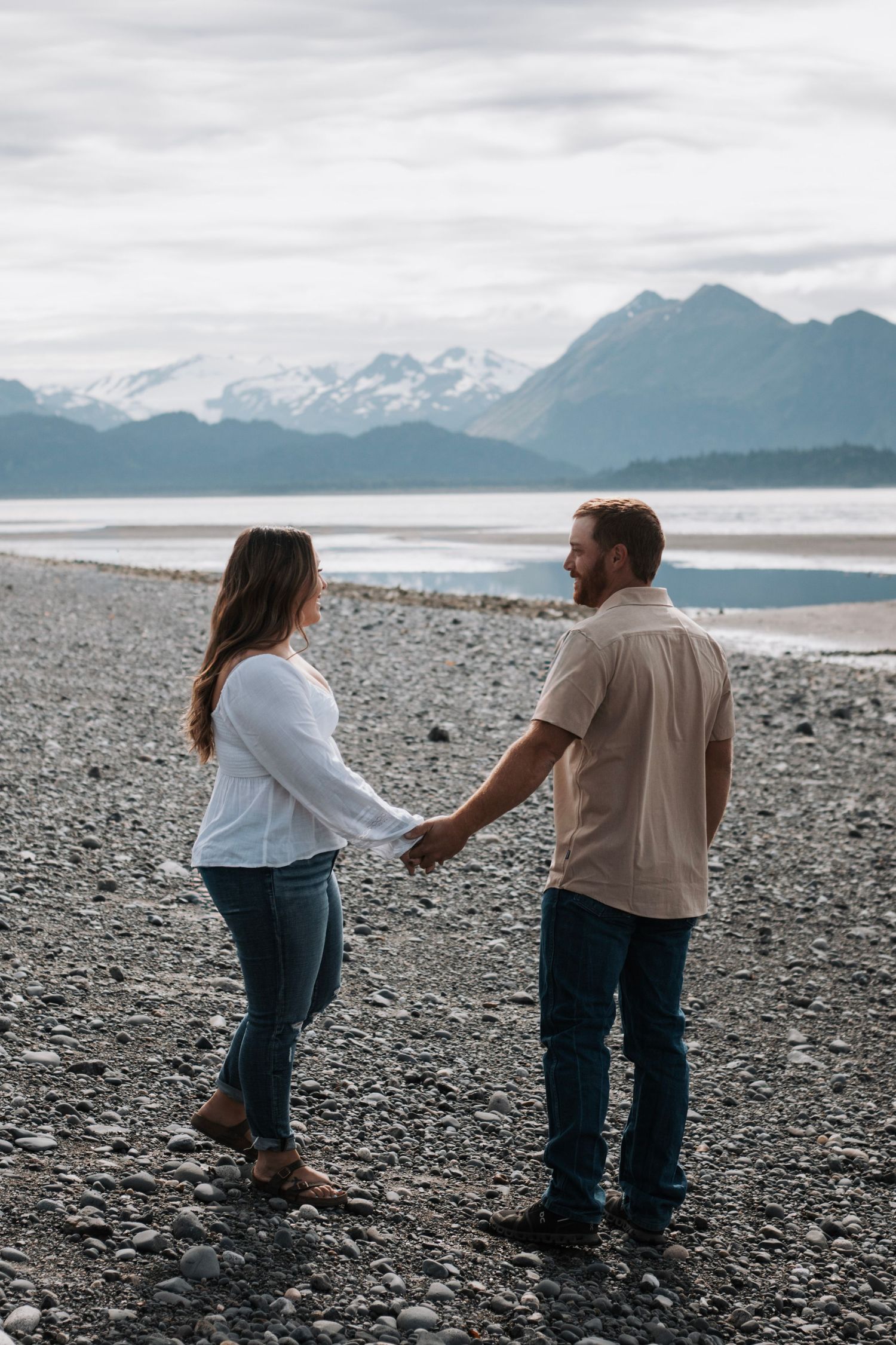 Scenic beach engagement session with snow-capped mountains in the background on rocky shore in Alaska