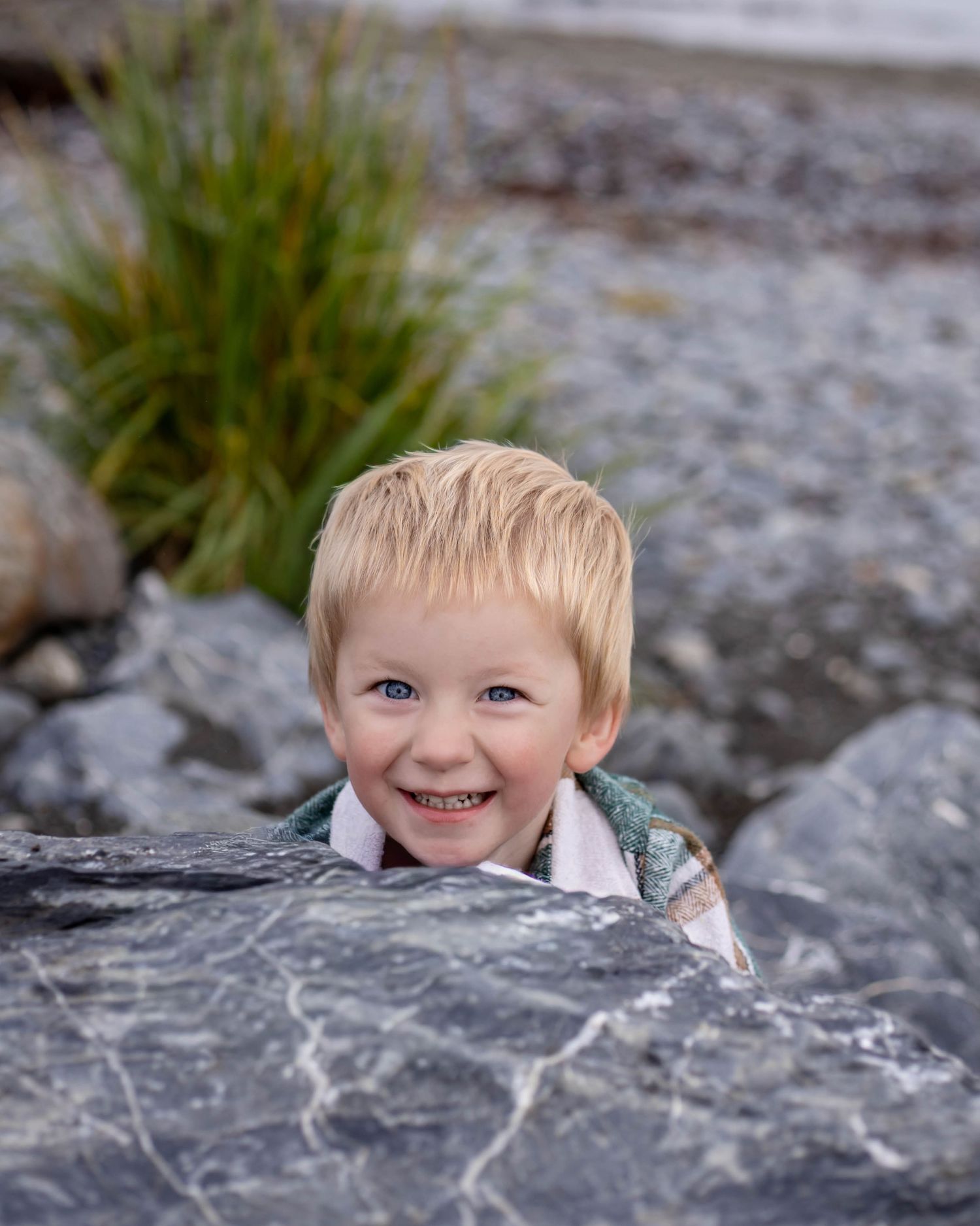 A child peeks playfully from behind a large gray rock formation.