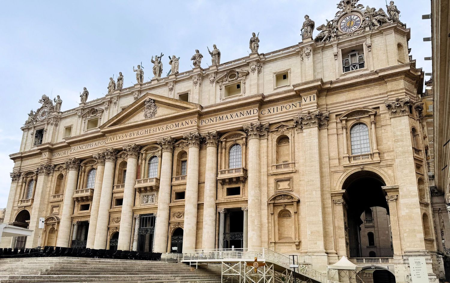 Wide panoramic view of Saint Peter's Basilica at Vatican City with ornate Baroque architecture and statues atop the facade.
